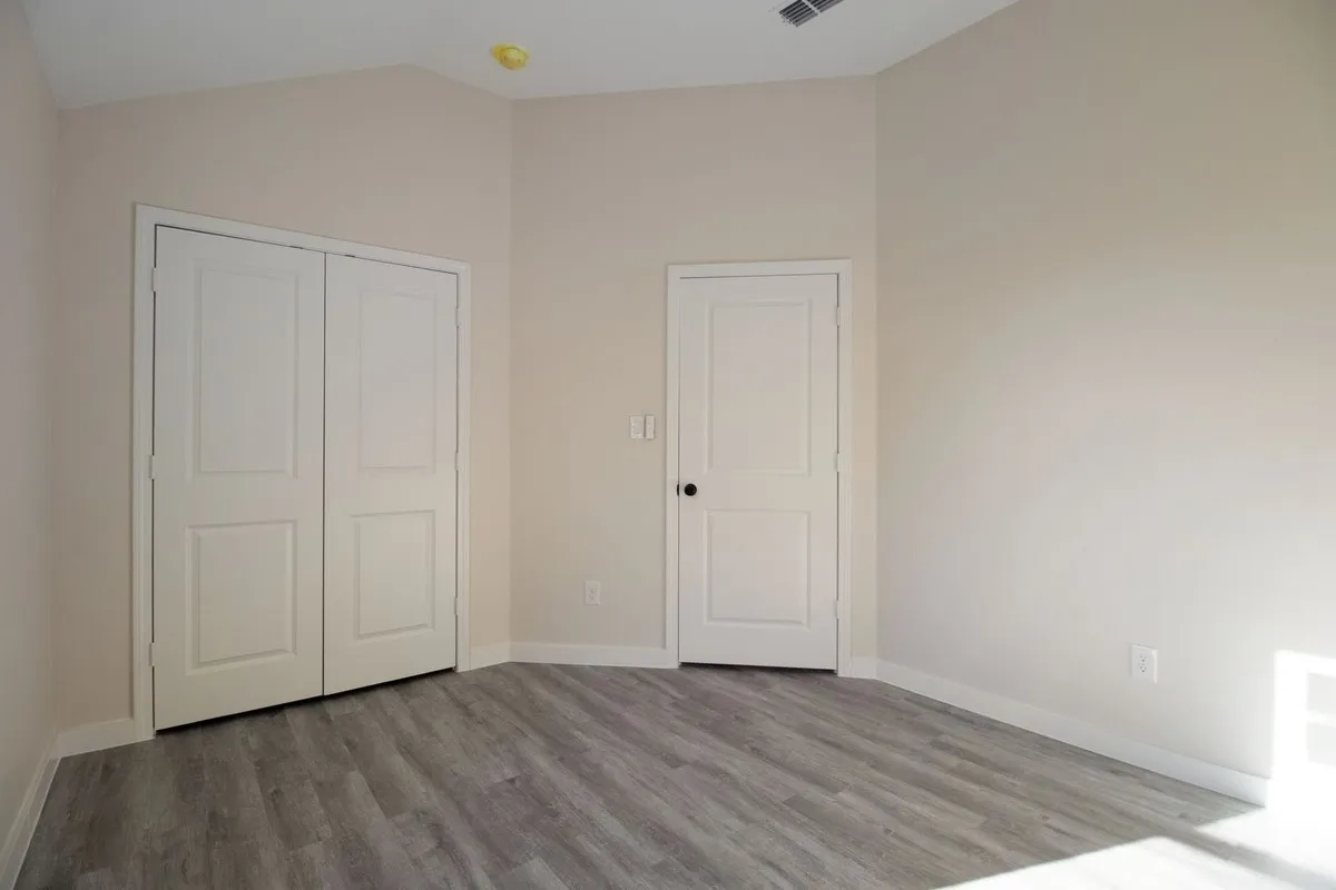 Vaulted ceiling, two-panel interior doors, light gray wood-finish flooring, and crisp white baseboards