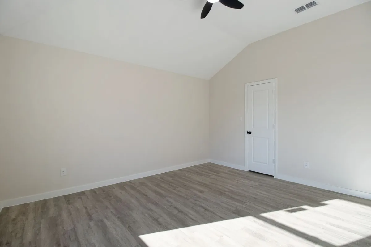 Vaulted ceiling, wood-finish flooring, white paneled door with black hardware, neutral wall paint, and ceiling fan
