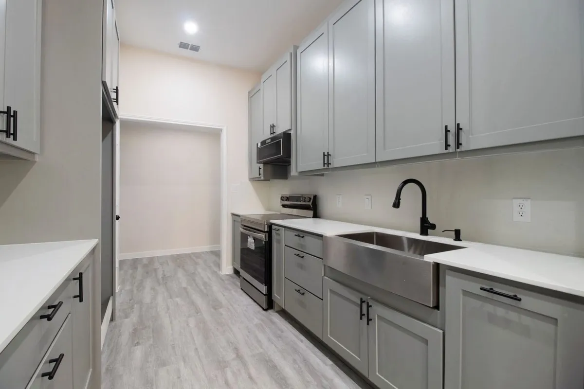 Wood-finish flooring, white countertops, stainless steel farmhouse sink, matte black faucet, and modern gray cabinetry