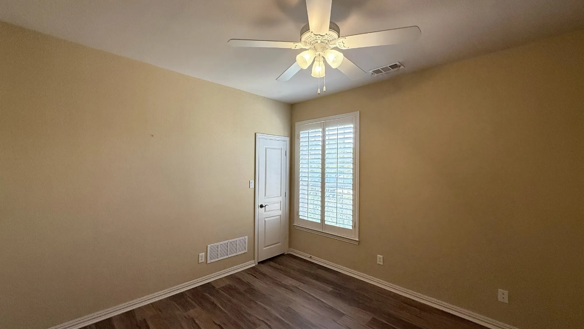 Wood-finish flooring, plantation shutters, ceiling fan with light fixture, and a solid core door