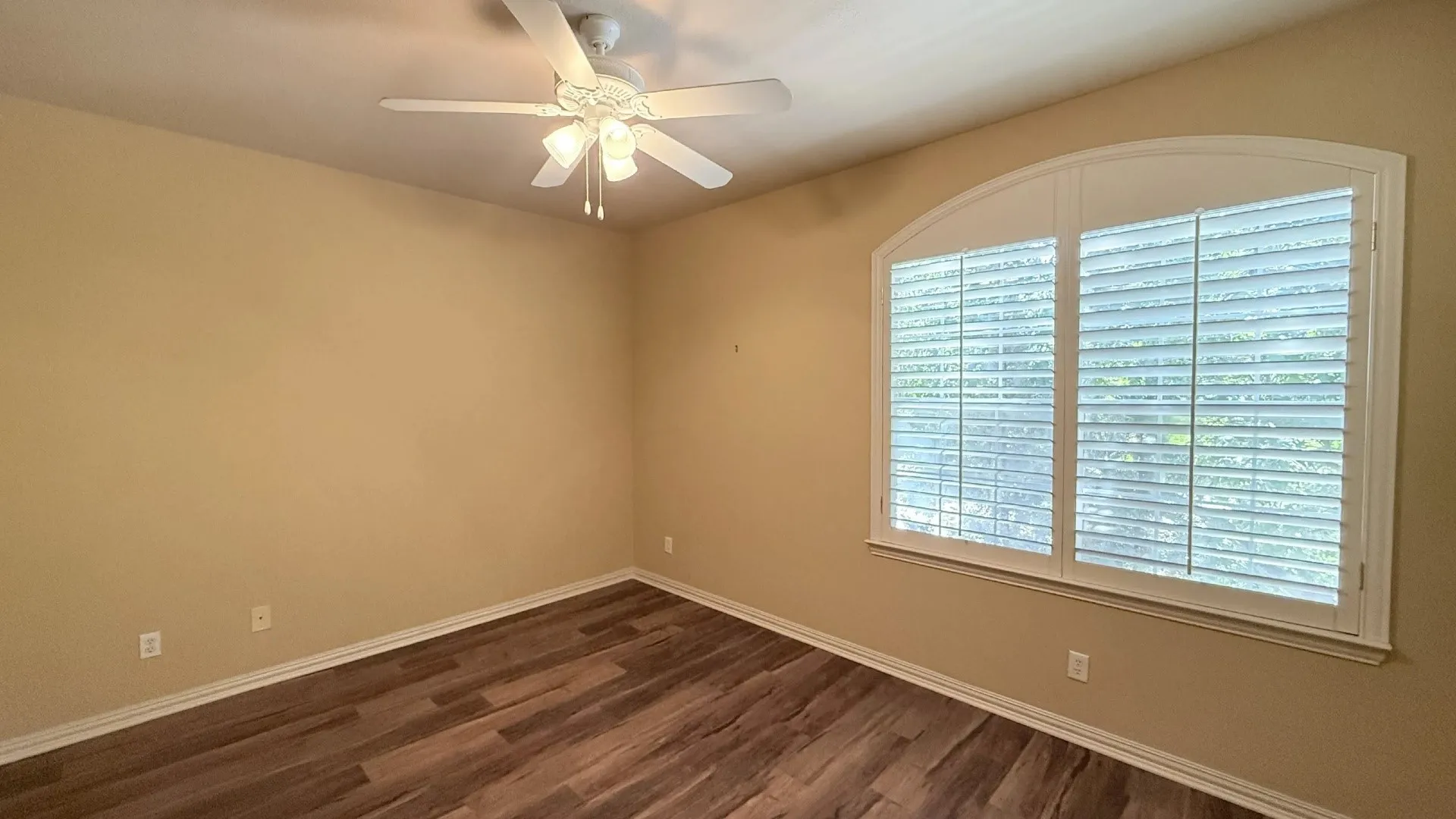 Wood-finish flooring, overhead ceiling fan with light fixture, and arched window with plantation shutters