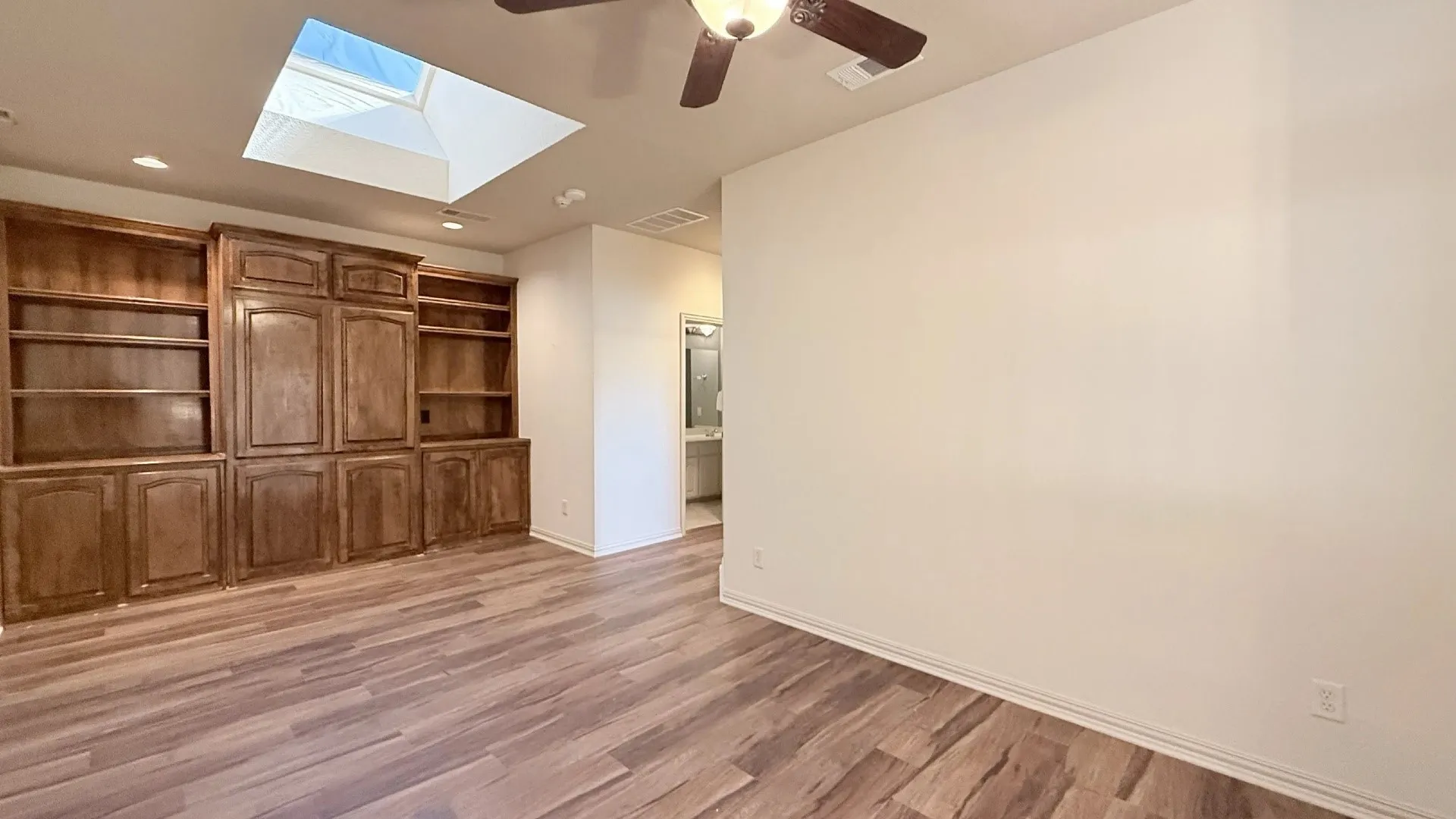 Wood-finish flooring, built-in cabinetry with shelving, recessed lighting, and a skylight