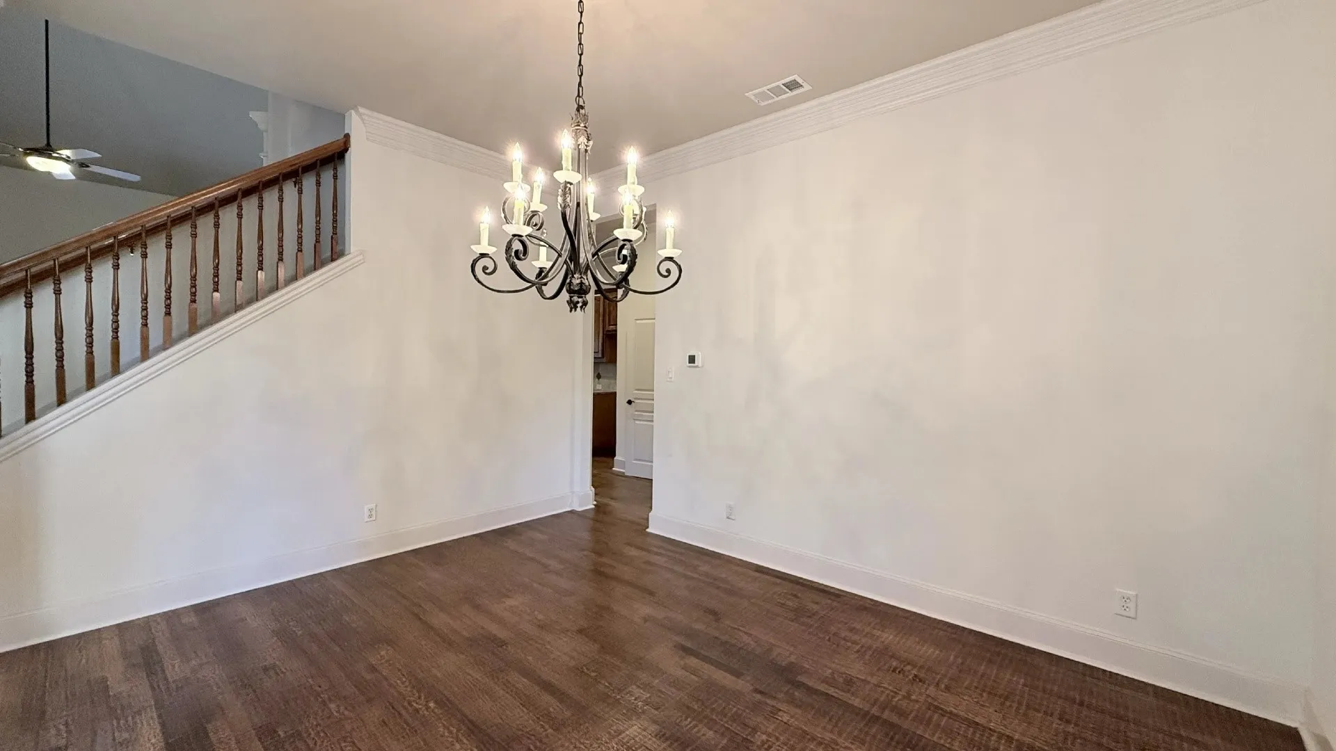 Dark wood-finish flooring, staircase with wood handrail, classic chandelier, and white crown molding