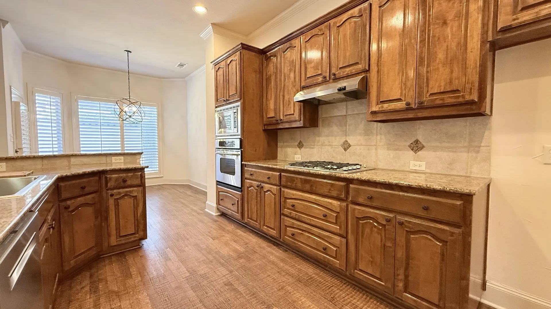 Wood-finish flooring throughout, wood cabinetry, stone countertops, stainless steel appliances, and a tile backsplash