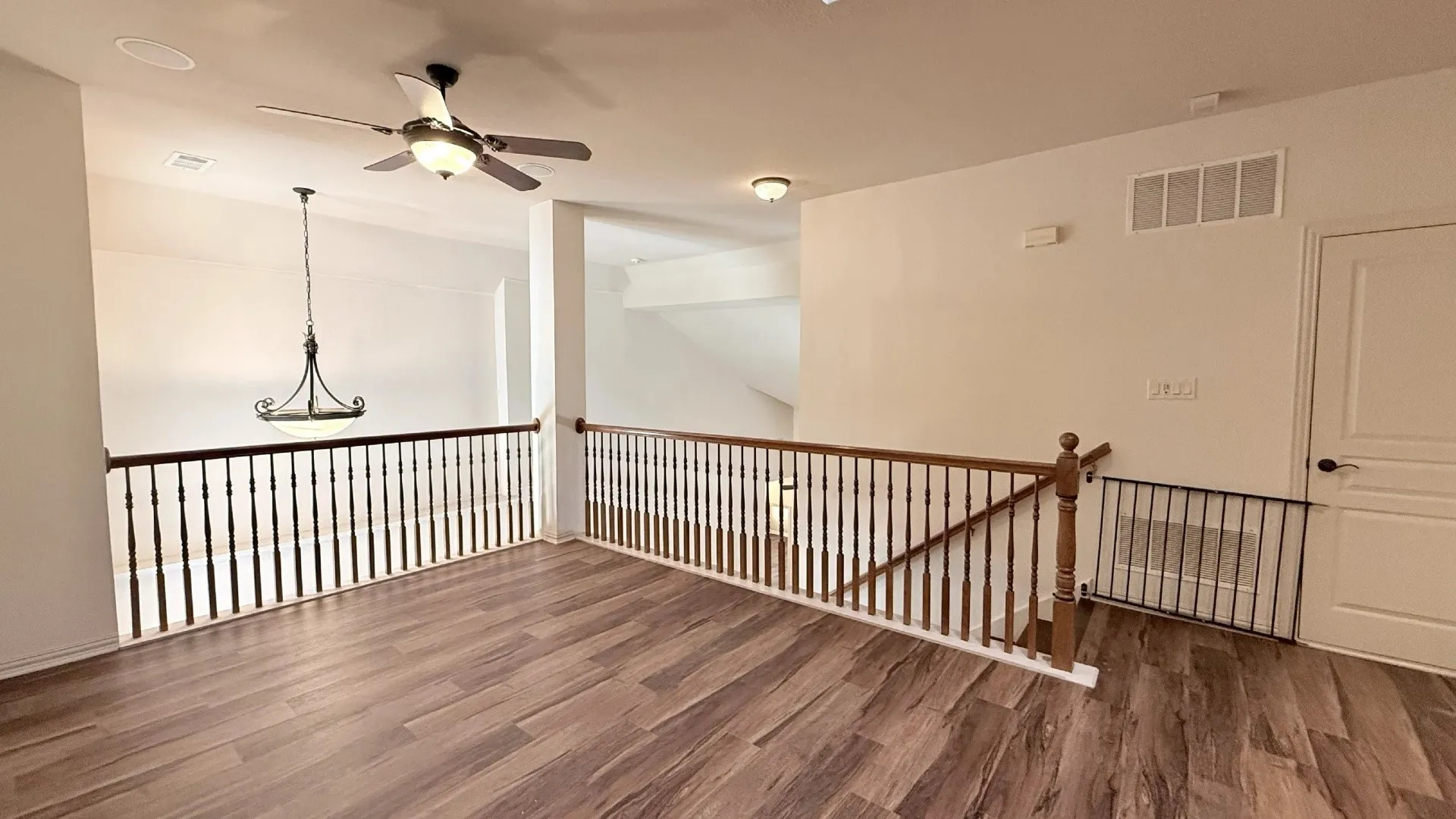 Wood-finish flooring, white walls, dark wood balusters, a ceiling fan, and an overhead light fixture