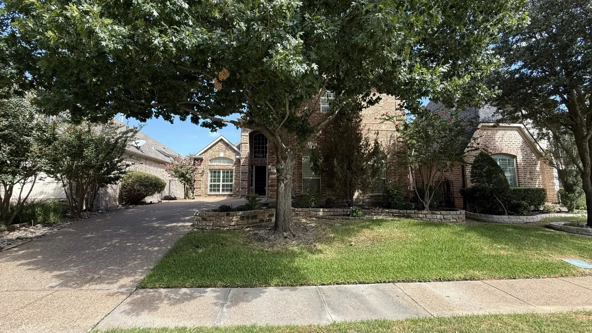 Brick exterior with stone accents, arched entry, mature trees, and a concrete driveway