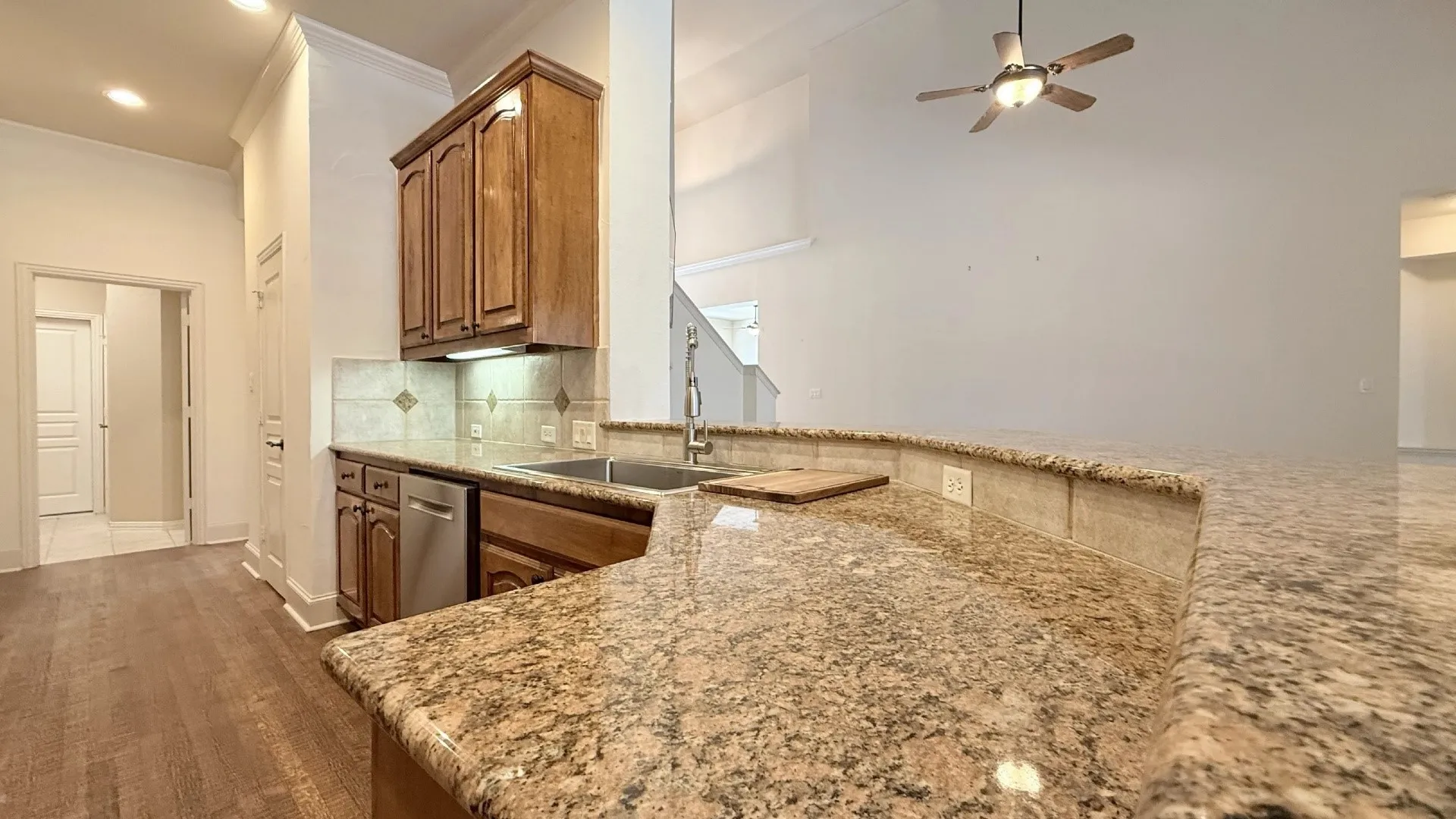 Kitchen featuring granite countertops, wood-finish flooring, stainless steel dishwasher, wood cabinetry, and a tile backsplash