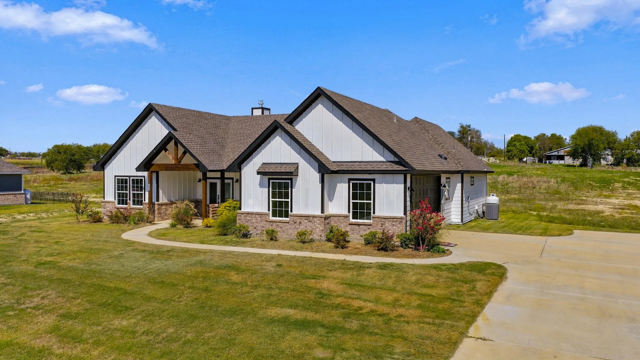 Single-story residence featuring white vertical siding, stone masonry skirting, a covered entryway with exposed timber trusses, and an attached garage