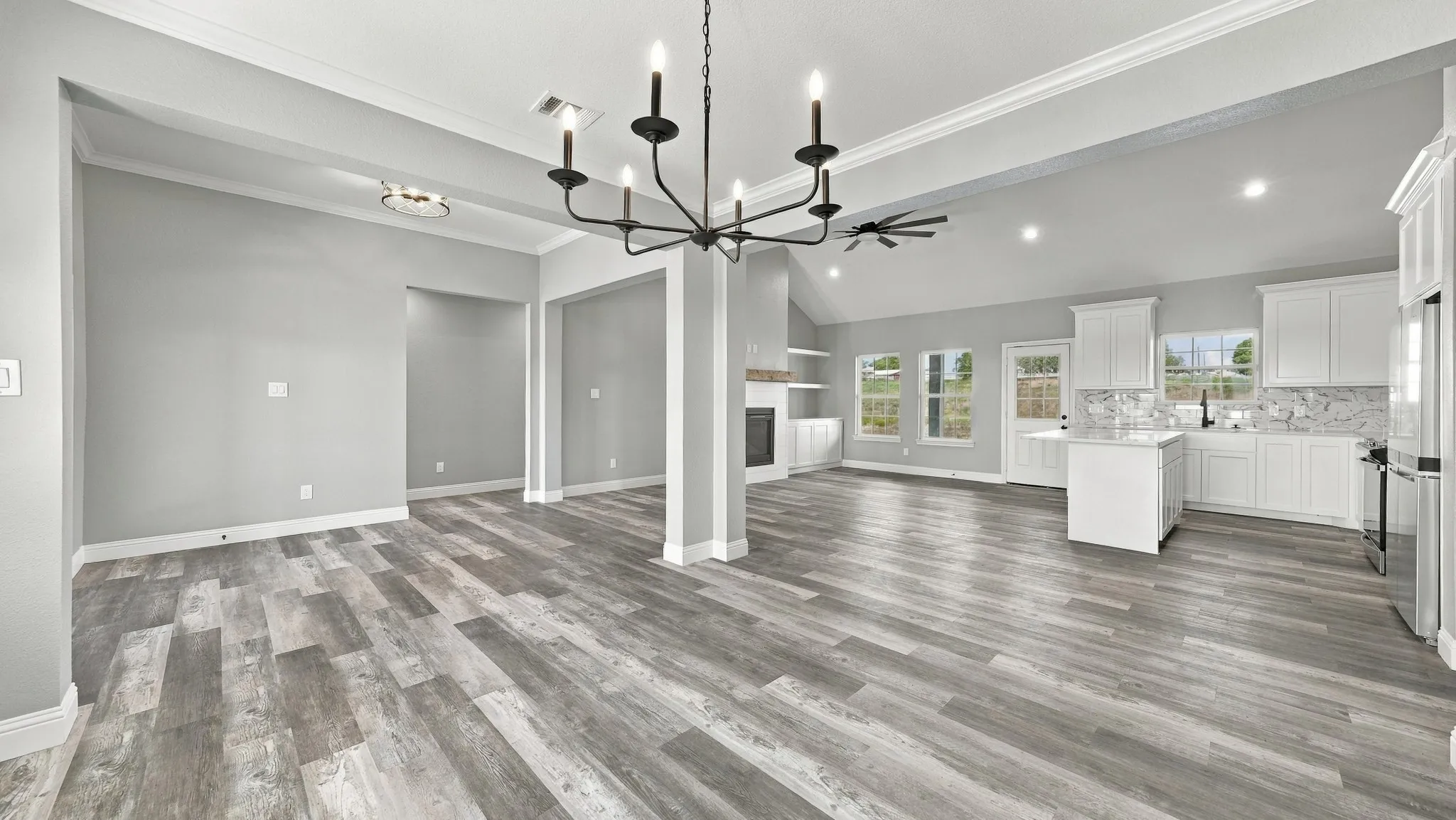 Open floor plan featuring wood-finish flooring, vaulted ceilings, a kitchen with white cabinetry and an island, a central chandelier, and a built-in fireplace