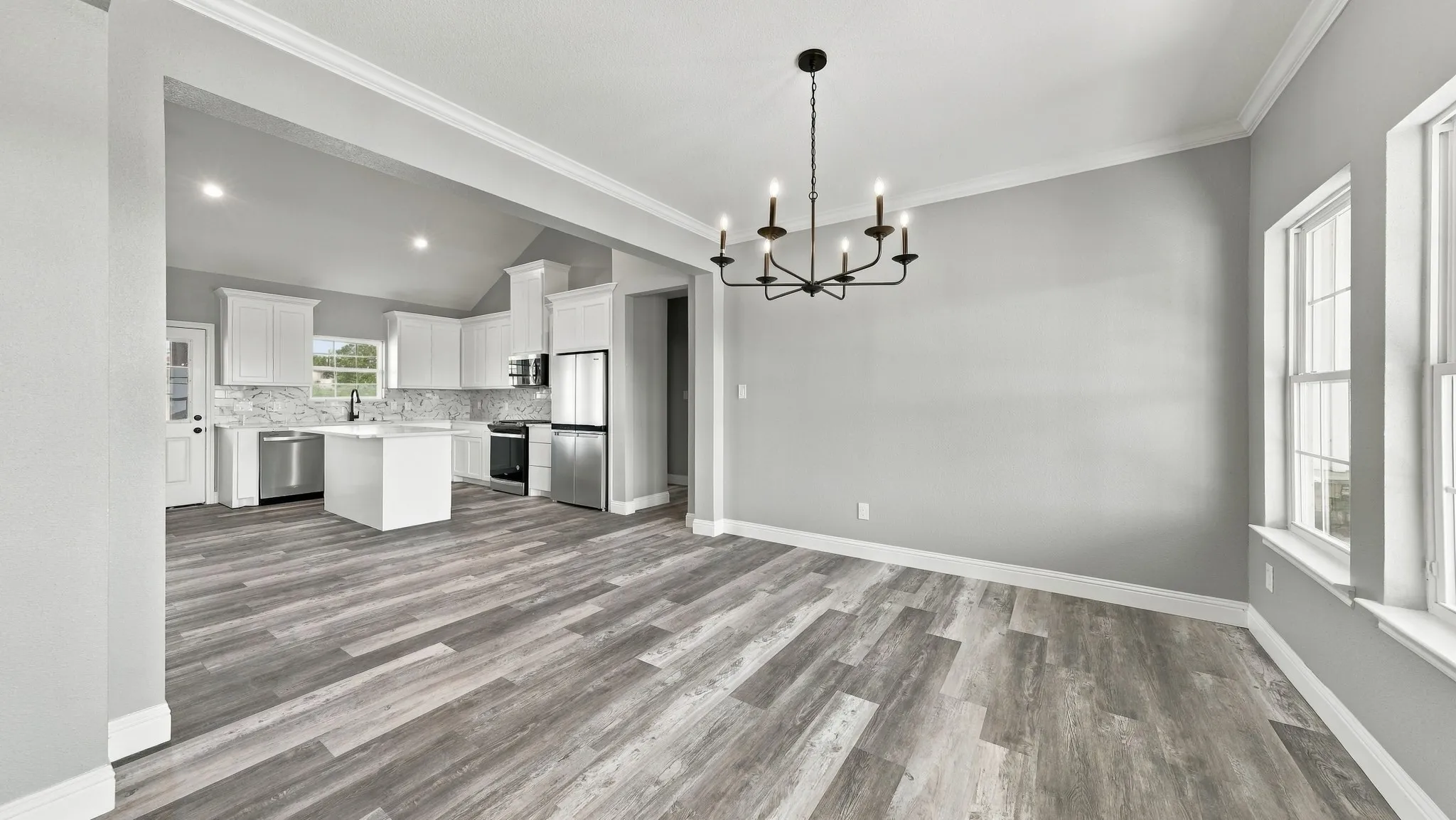 Open-concept interior featuring wood-finish flooring, a multi-arm chandelier, vaulted ceilings, white cabinetry, and a center kitchen island