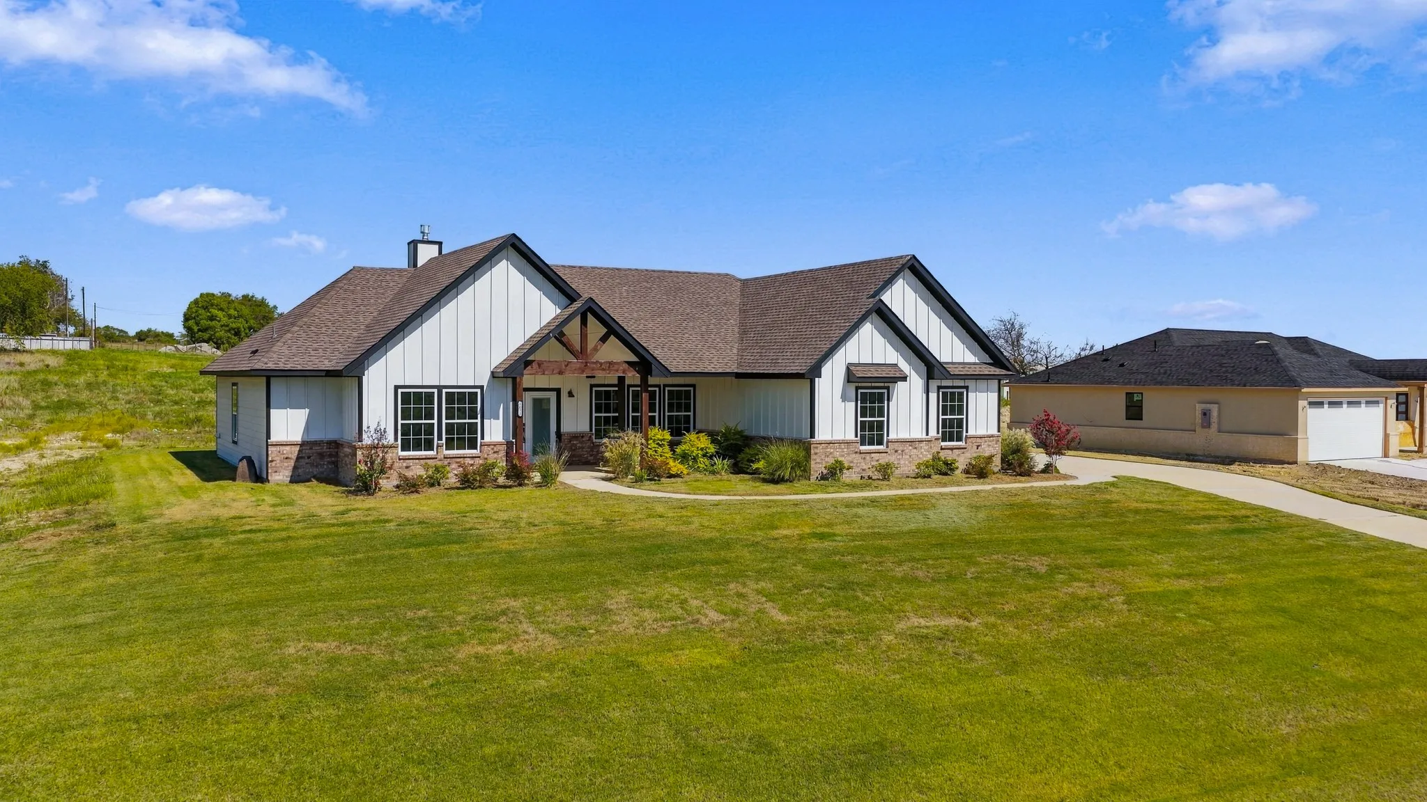 Modern farmhouse exterior featuring vertical board-and-batten siding, stone masonry accents, a timber-frame covered entryway, and a concrete driveway