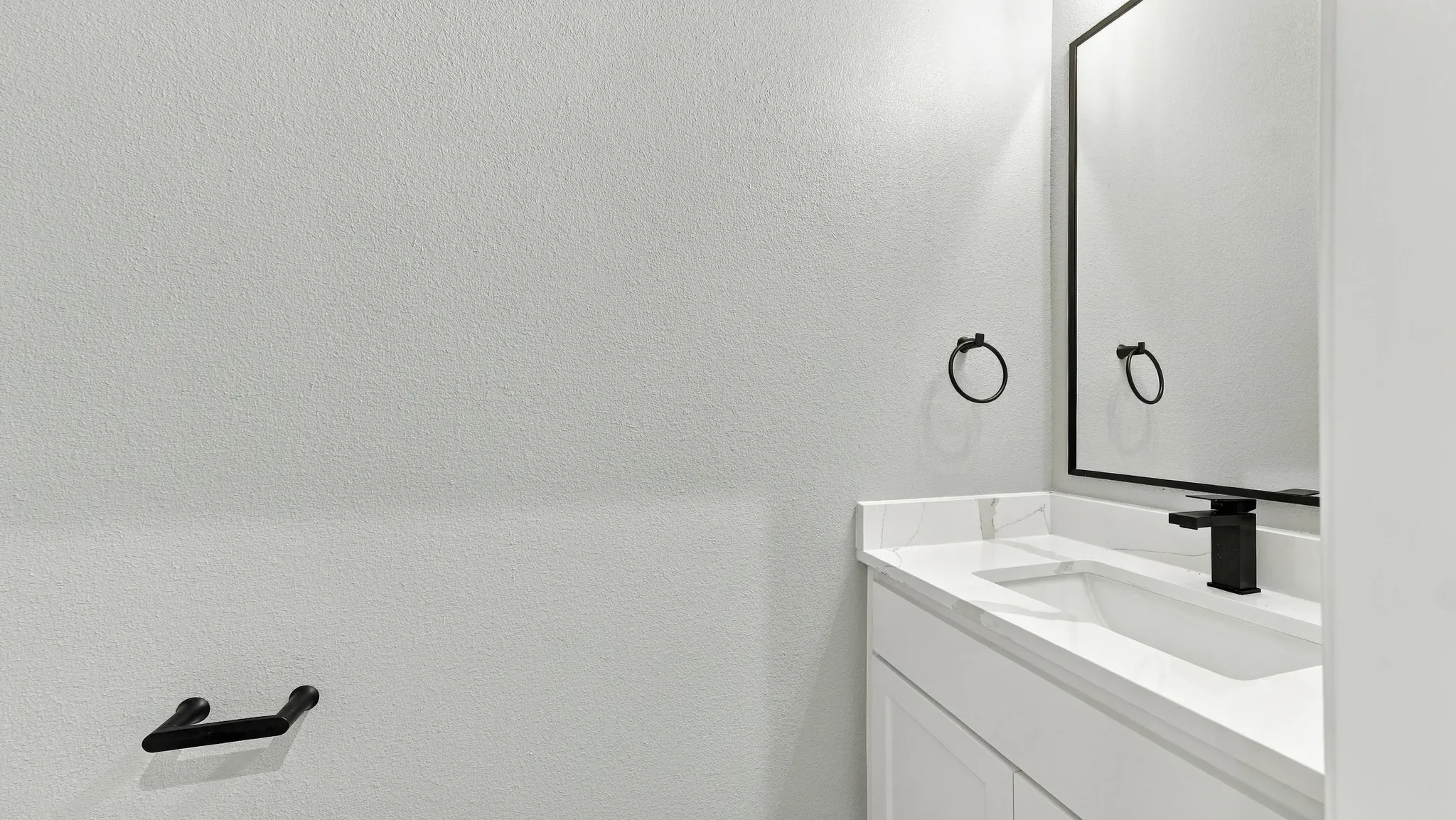 Bathroom vanity with a white countertop and integrated sink, featuring a matte black faucet, a black-framed mirror, and matching matte black hardware