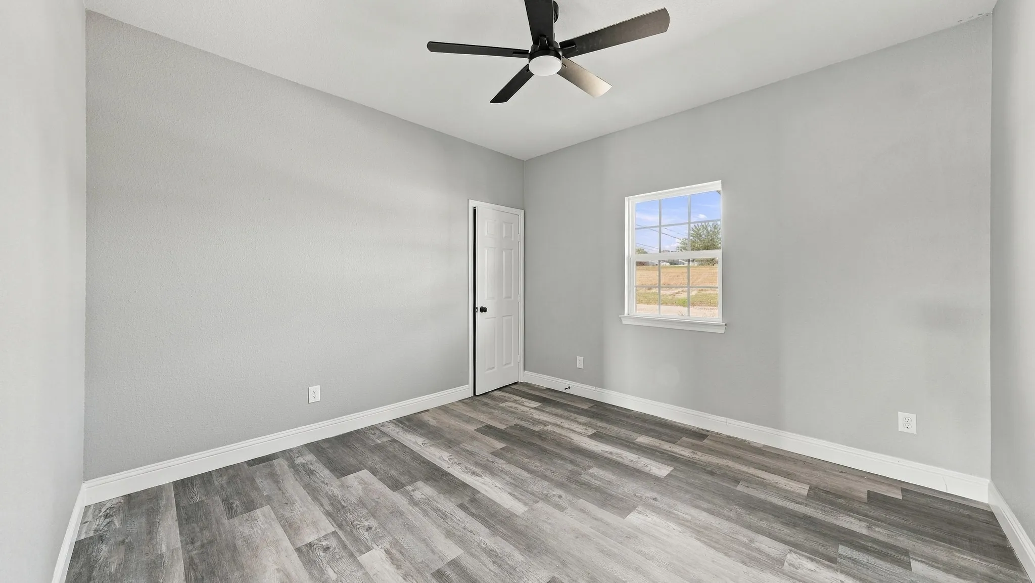 Neutral-toned interior space featuring wood-finish flooring, a ceiling fan with integrated lighting, and a single-hung window with muntins