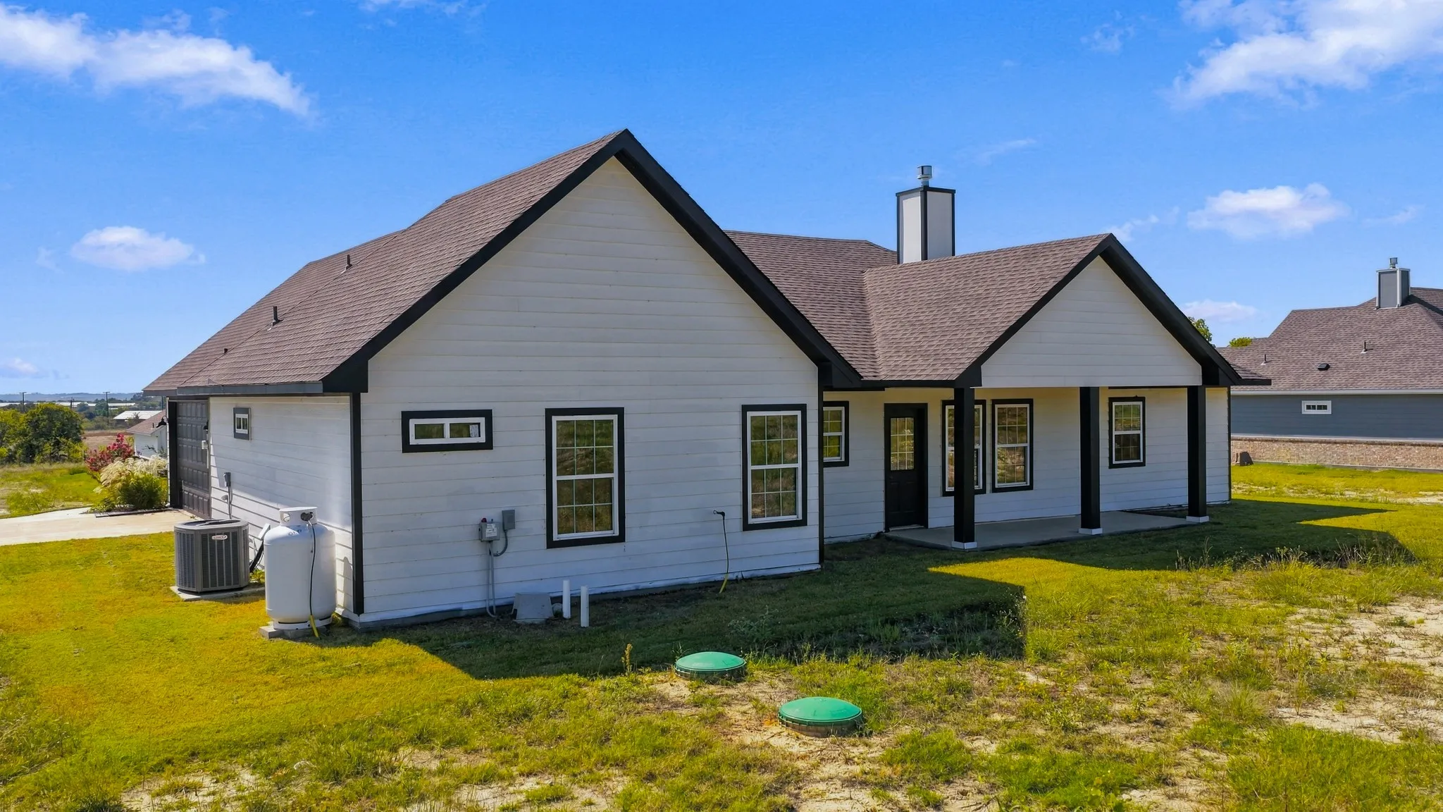 Single-story residence featuring horizontal lap siding, a pitched asphalt shingle roof, a covered concrete patio, and a central chimney stack