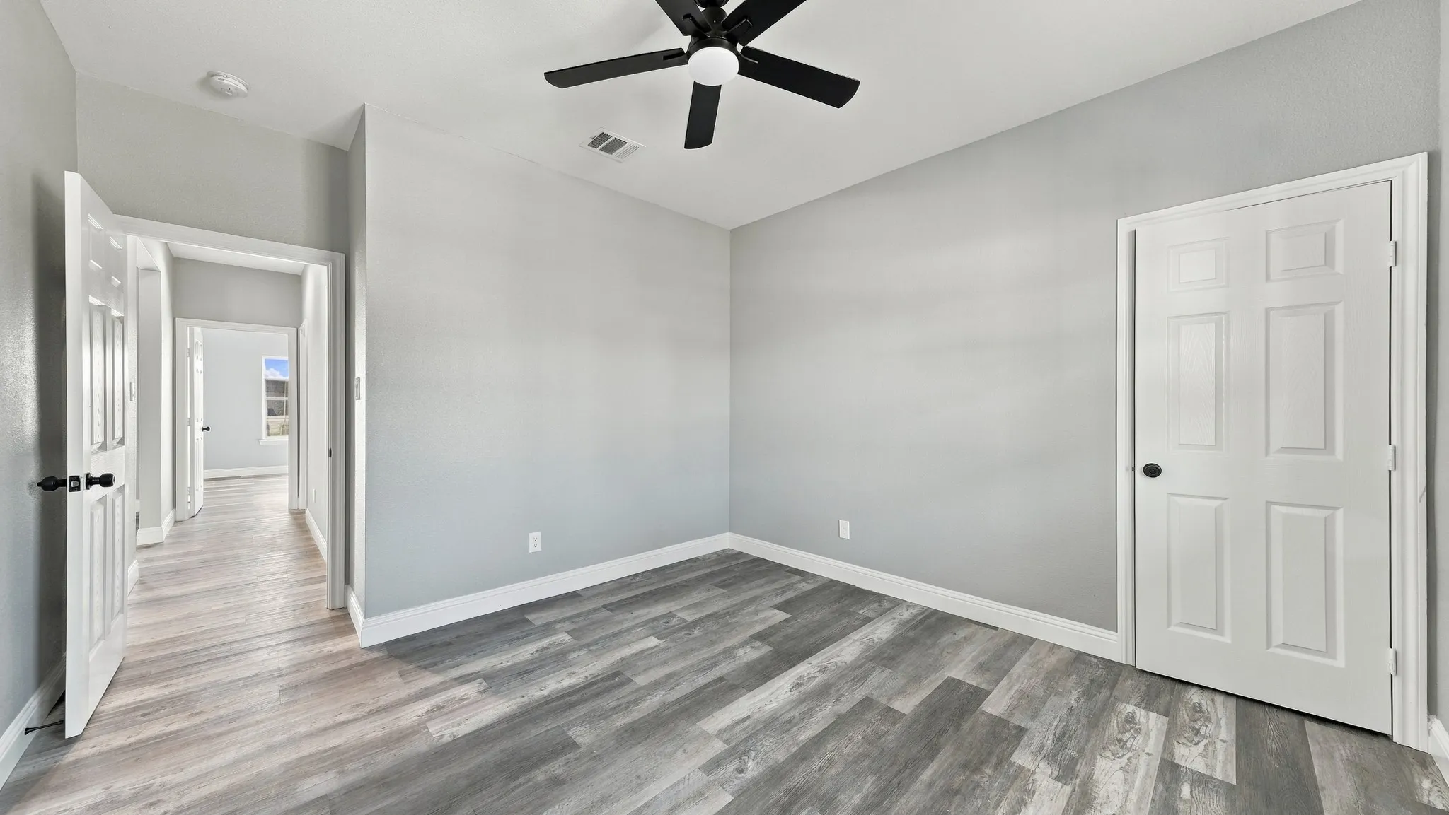 Neutral-toned interior featuring wood-finish flooring, a six-panel door, and a matte black ceiling fan