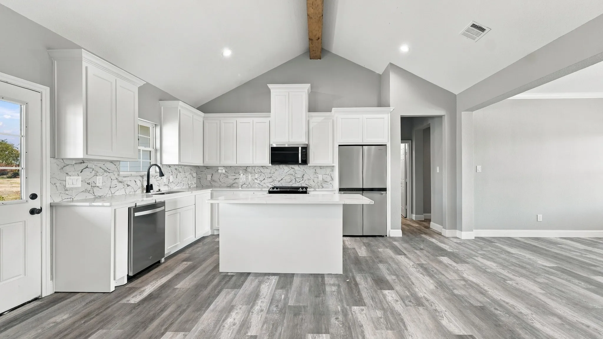 Kitchen featuring vaulted ceilings with exposed wood beam, white cabinetry, a center island, stone-patterned backsplash, and wood-finish flooring