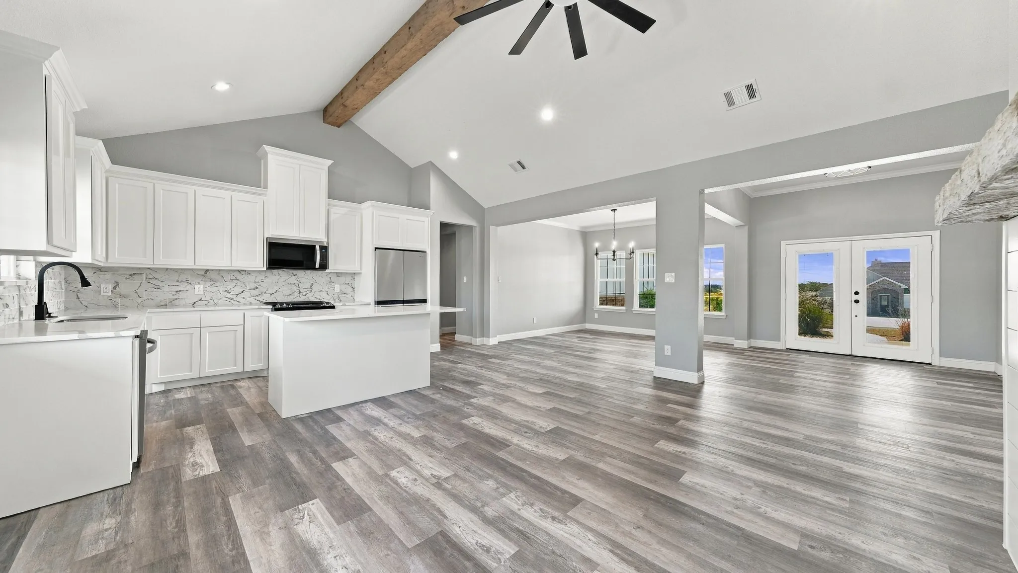Vaulted ceilings with exposed wooden beam, white cabinetry, solid surface countertops, patterned tile backsplash, and wood-finish flooring