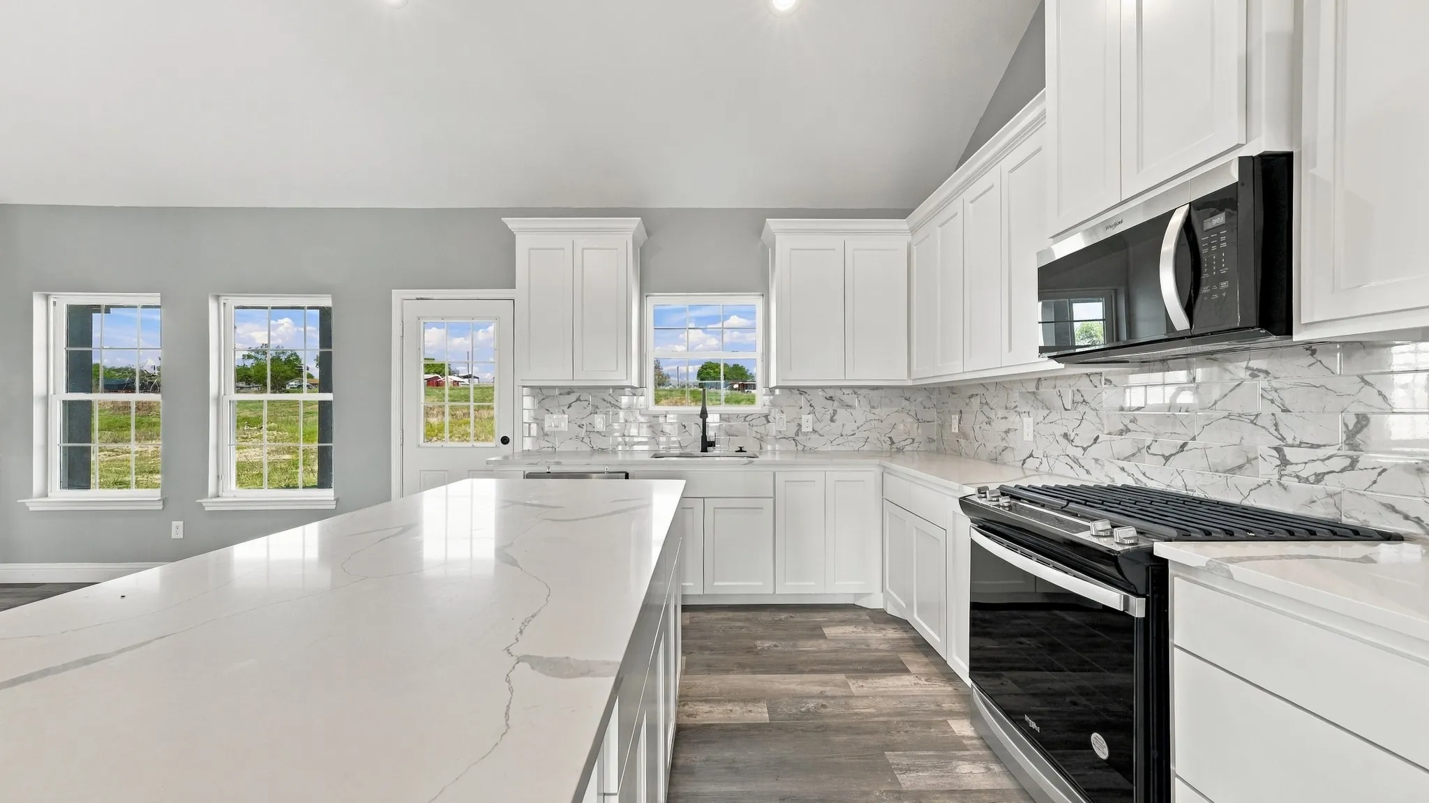 Kitchen featuring white shaker-style cabinetry, quartz countertops with a veined pattern, stone-finish backsplash, wood-finish flooring, and black appliances