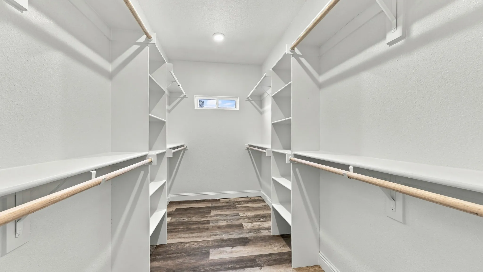 Walk-in closet featuring white built-in shelving, wooden garment rods, wood-finish flooring, and a window