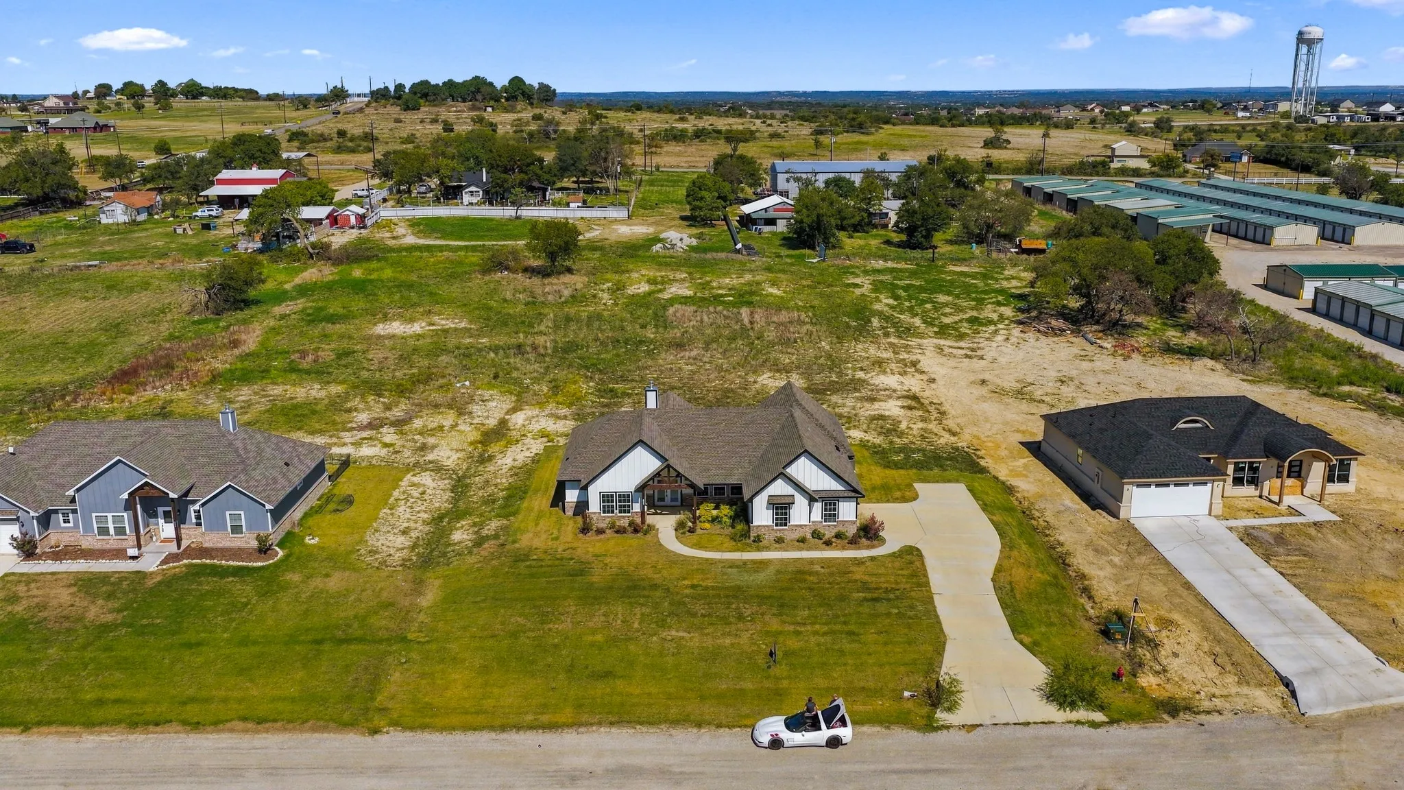 Aerial perspective of a single-story residence featuring a multi-gabled roofline, stone and stucco exterior, concrete driveway, and expansive undeveloped acreage
