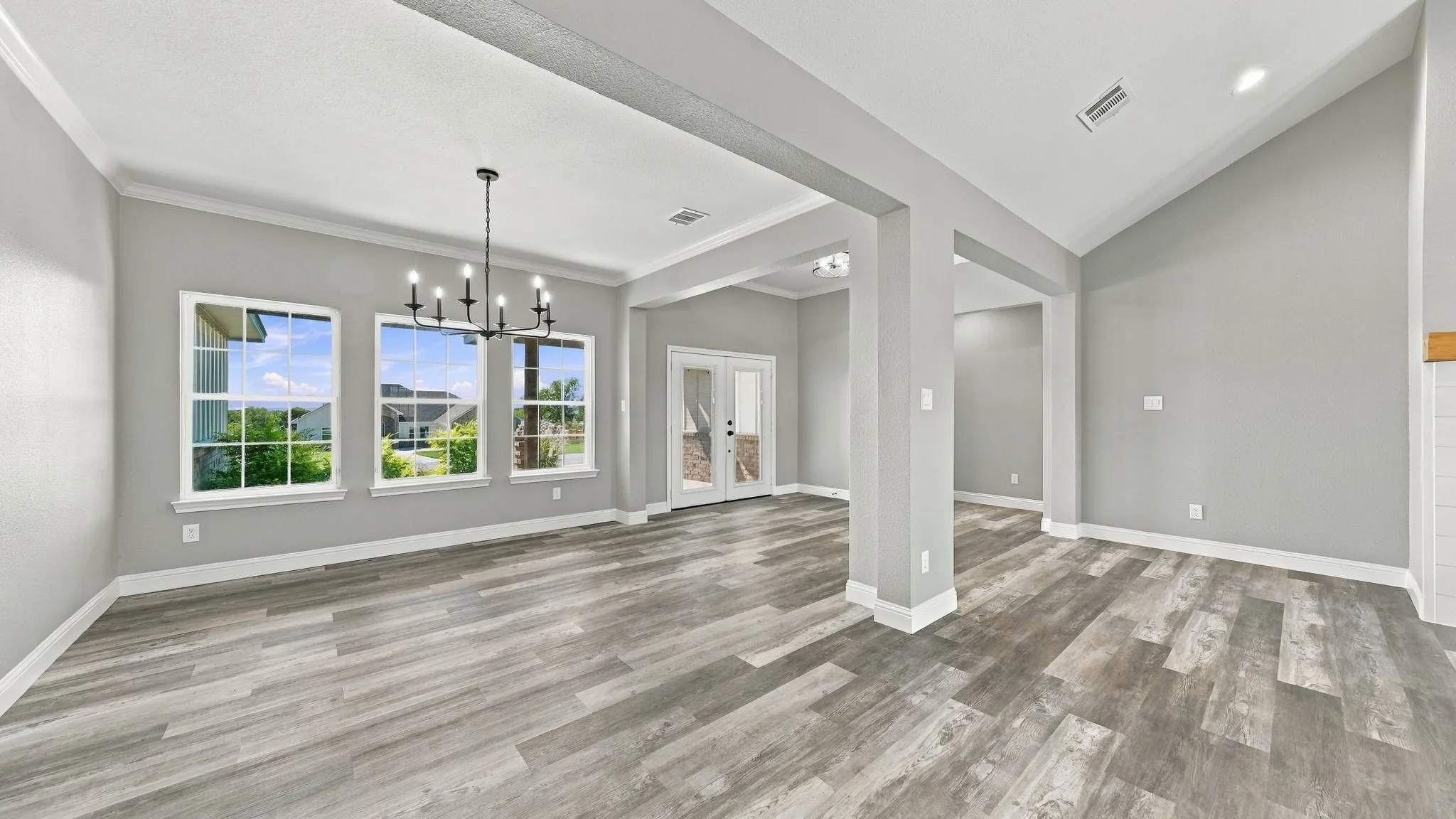 Open-concept interior featuring vaulted ceilings, wood-finish flooring, a multi-light chandelier, and large windows with grid muntins