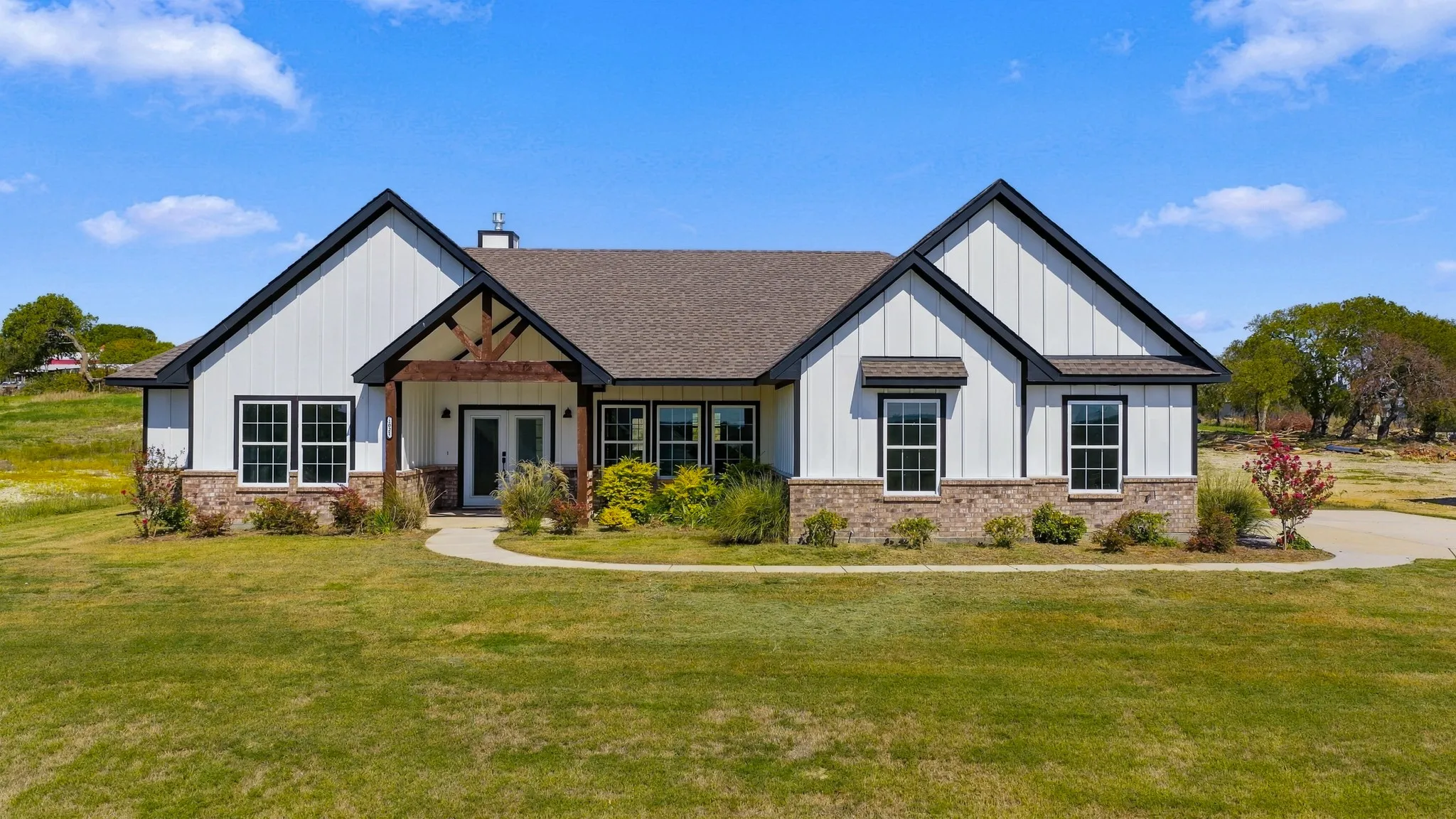 Modern farmhouse exterior featuring vertical board-and-batten siding, stone masonry veneer, a covered entryway with exposed timber trusses, and a multi-gabled roofline