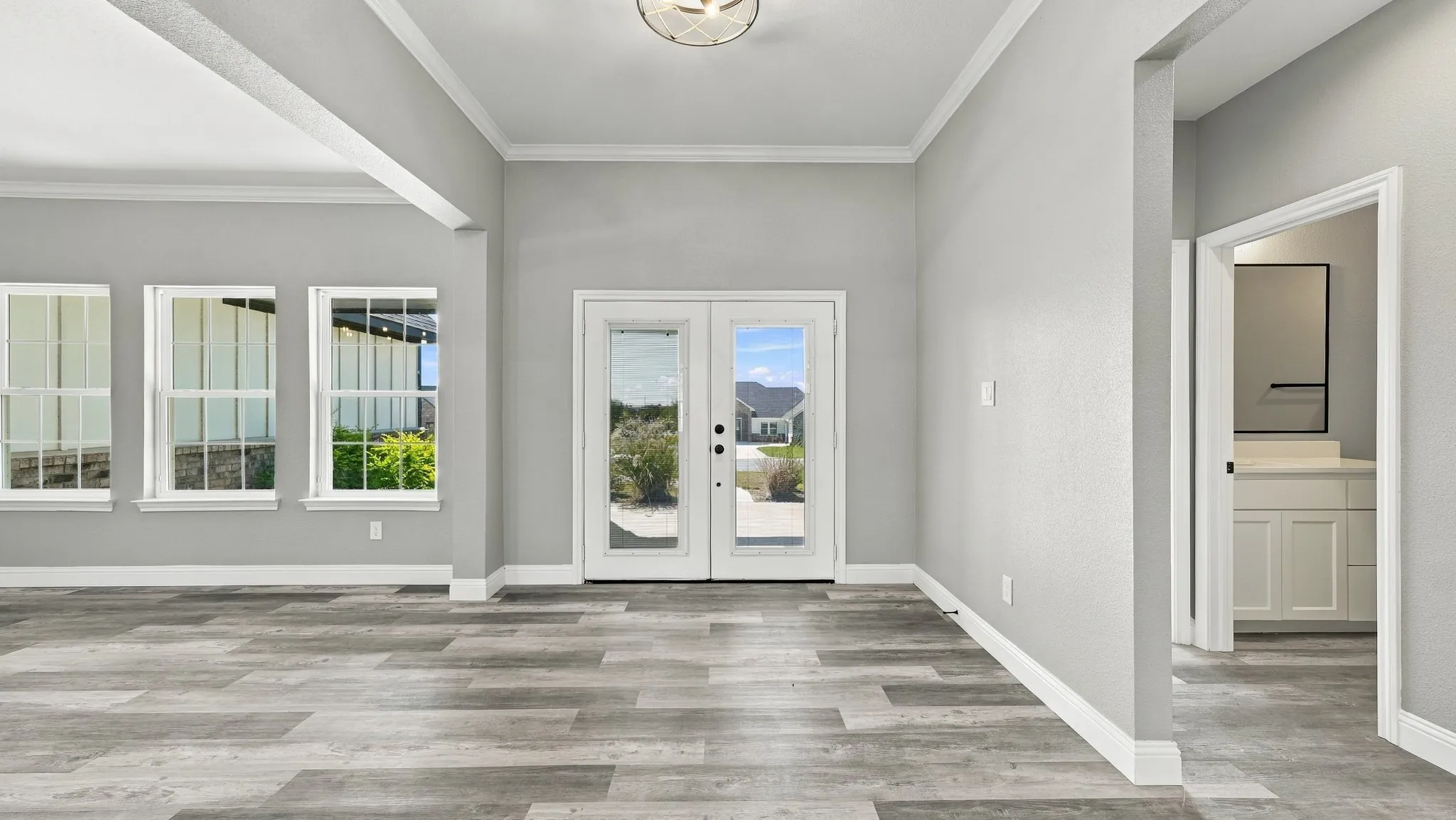 Interior space featuring wood-finish flooring, double glass-panel entry doors, three large windows, crown molding, and a flush-mount light fixture