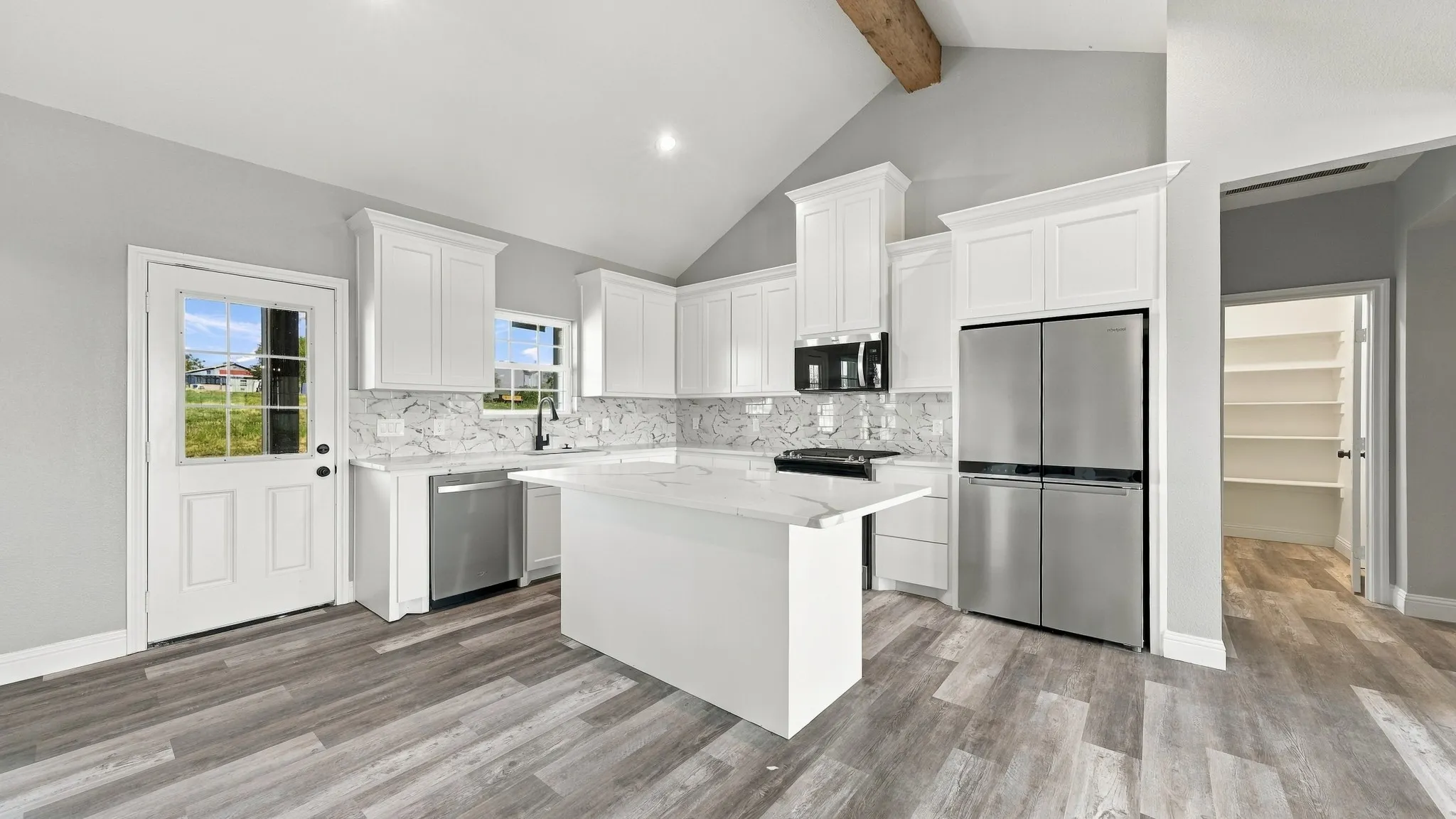 Kitchen featuring a vaulted ceiling with decorative wood beam, white cabinetry, stone-finish countertops and backsplash, stainless steel appliances, and wood-finish flooring
