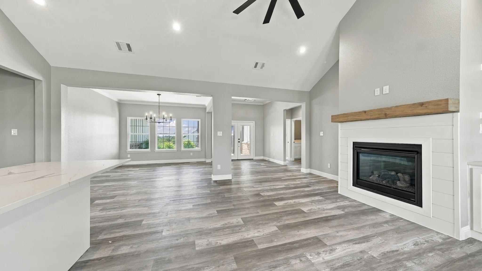 Vaulted ceiling featuring a central ceiling fan, fireplace with white shiplap surround and timber mantel, wood-finish flooring, and recessed lighting