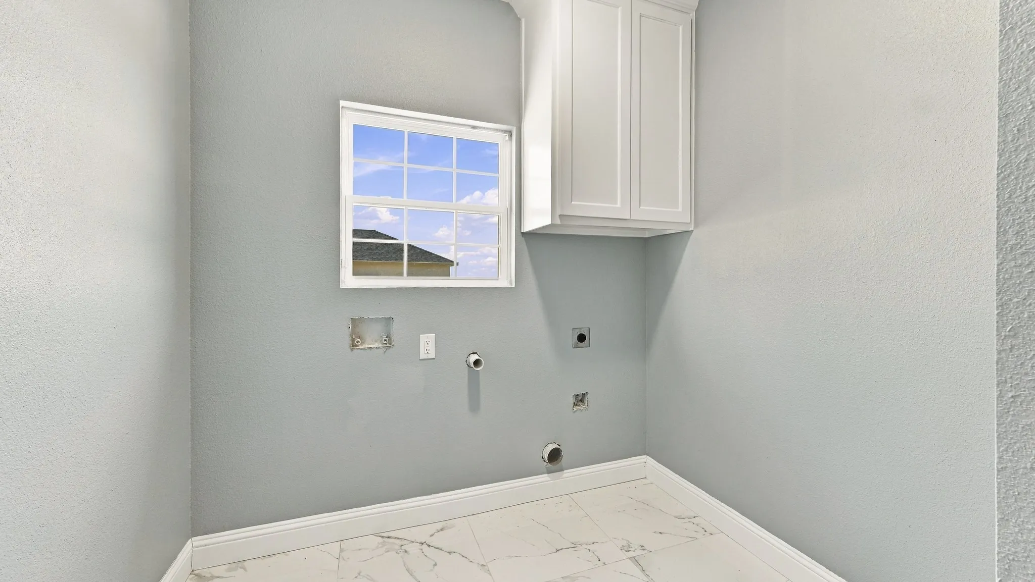Utility area featuring white built-in cabinetry, large-format tile flooring, and a single-hung window