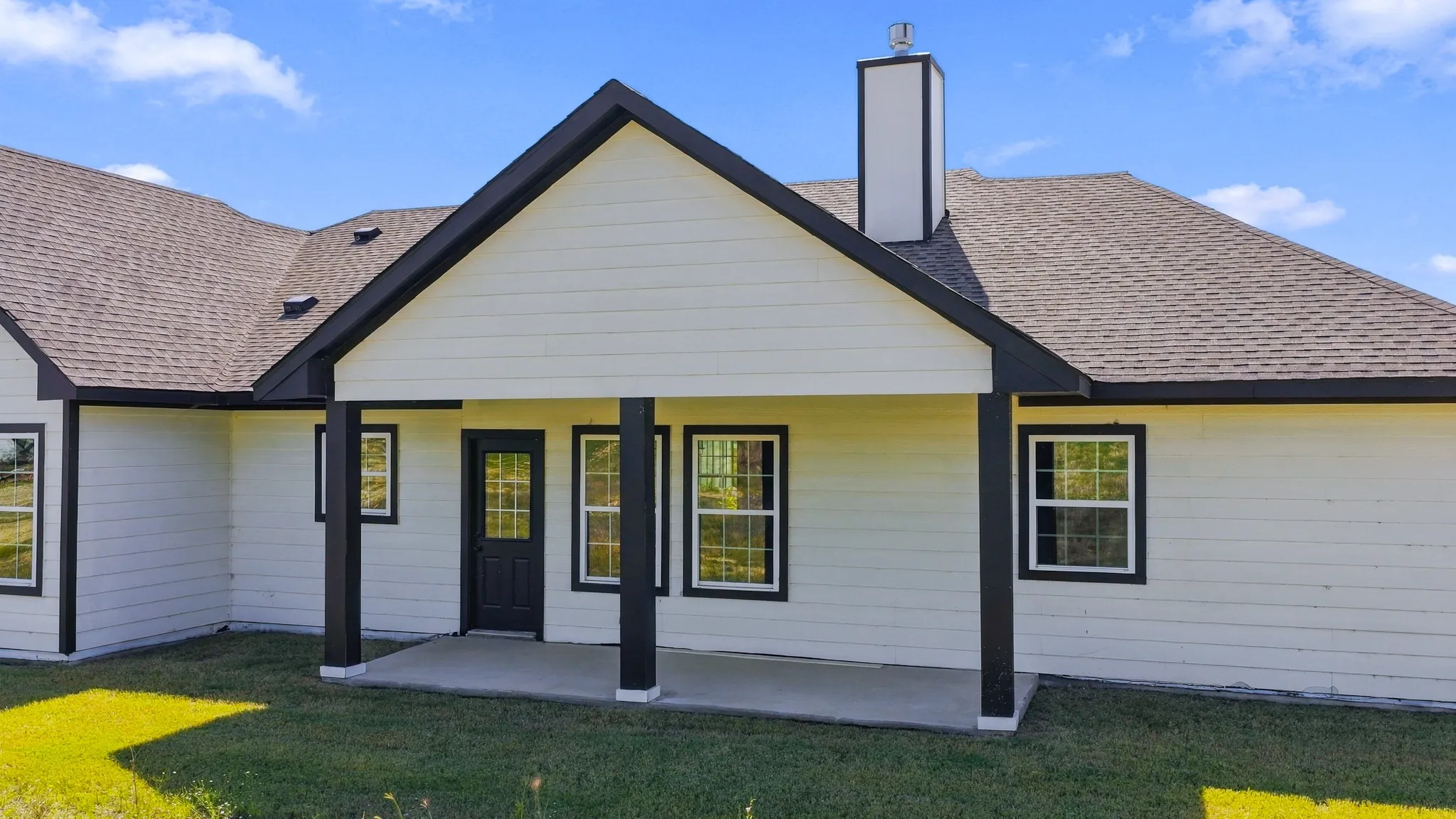 Exterior featuring horizontal lap siding, a covered concrete patio, a dual-pitched roofline with asphalt shingles, and a central chimney