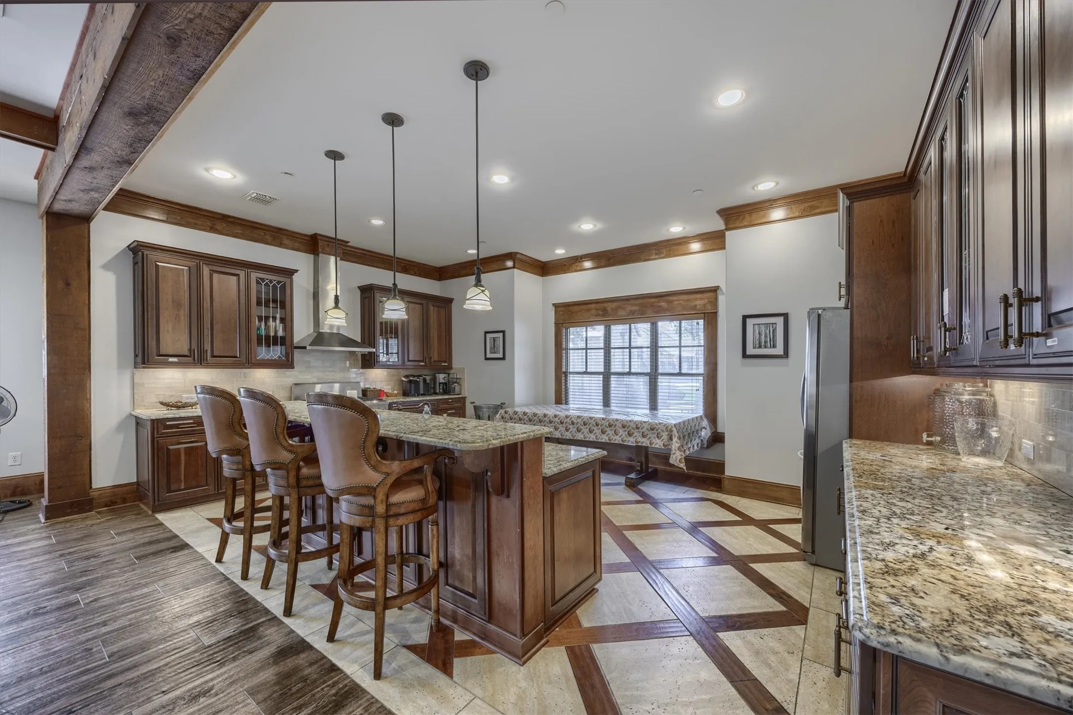 Expansive kitchen island, rich wood cabinetry, granite countertops, stainless steel range hood, and recessed lighting