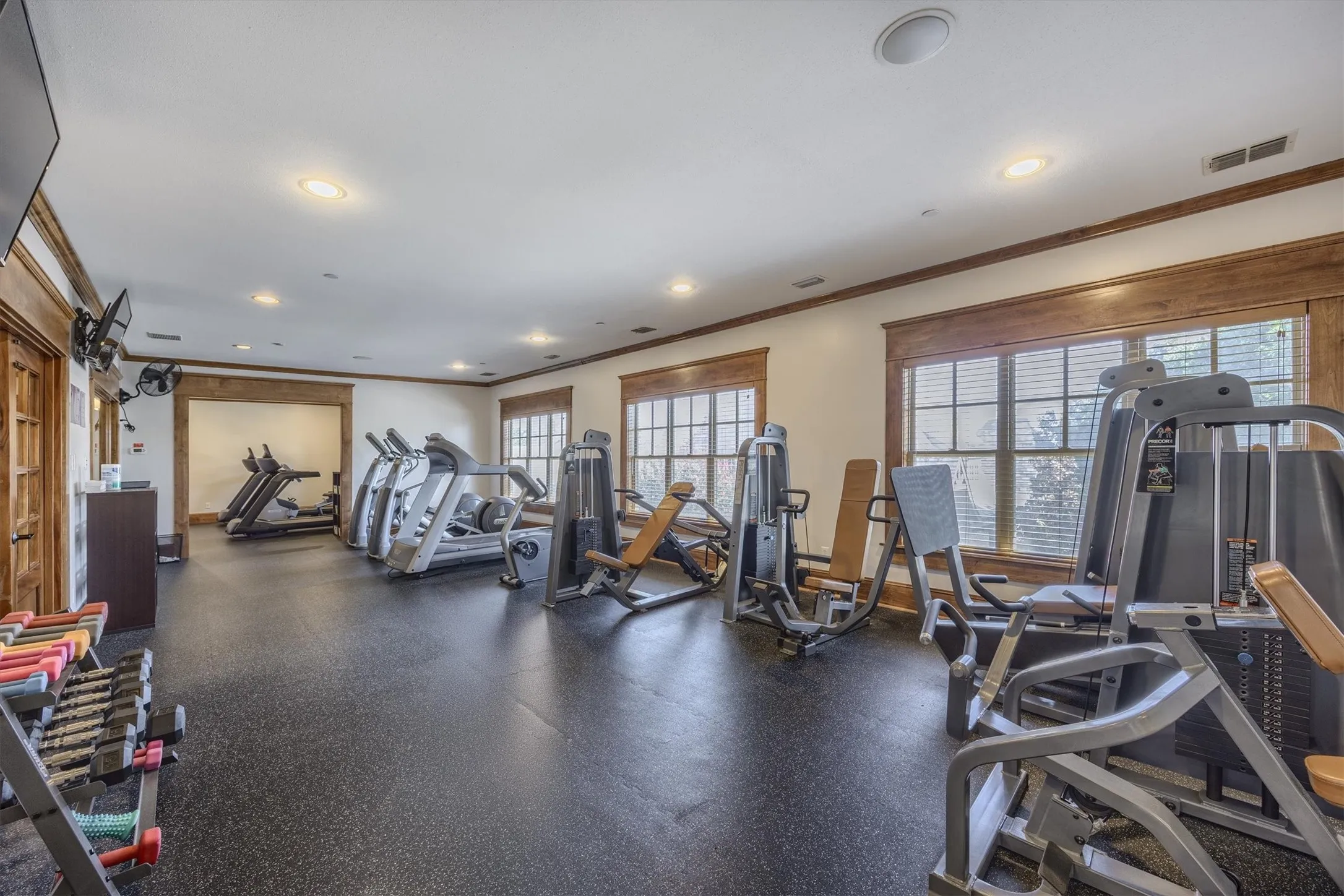 Interior fitness room featuring rubber flooring, multiple fitness machines, recessed lighting, and wood-trimmed windows
