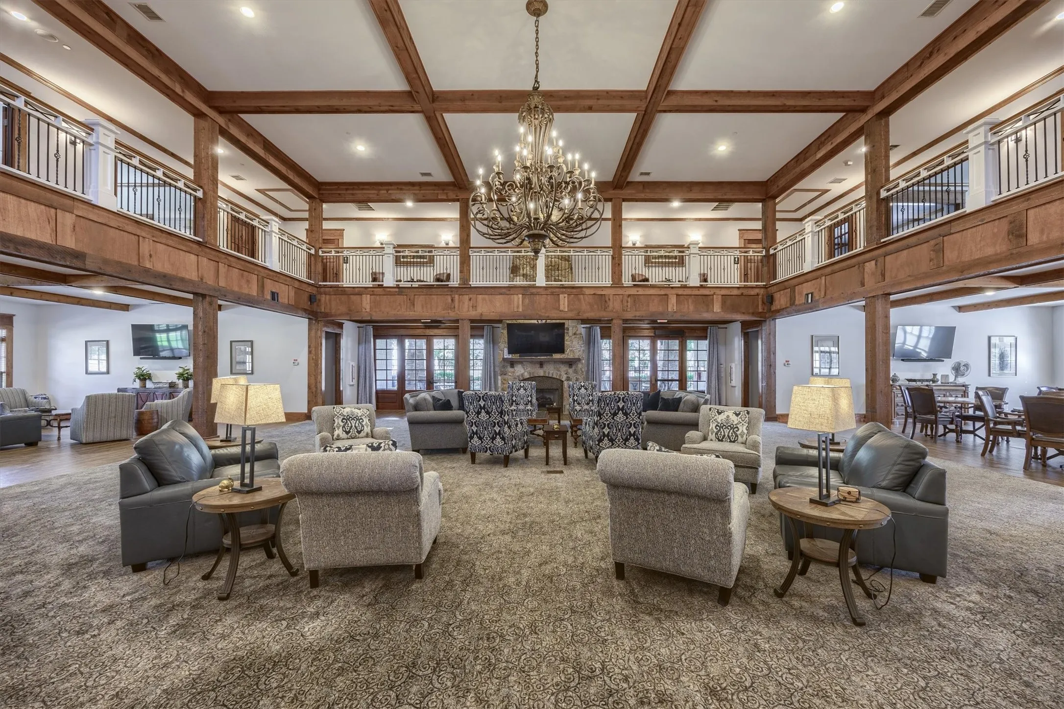 Two-story great room with exposed wood beams, a prominent chandelier, stone fireplace, and multiple sets of French doors