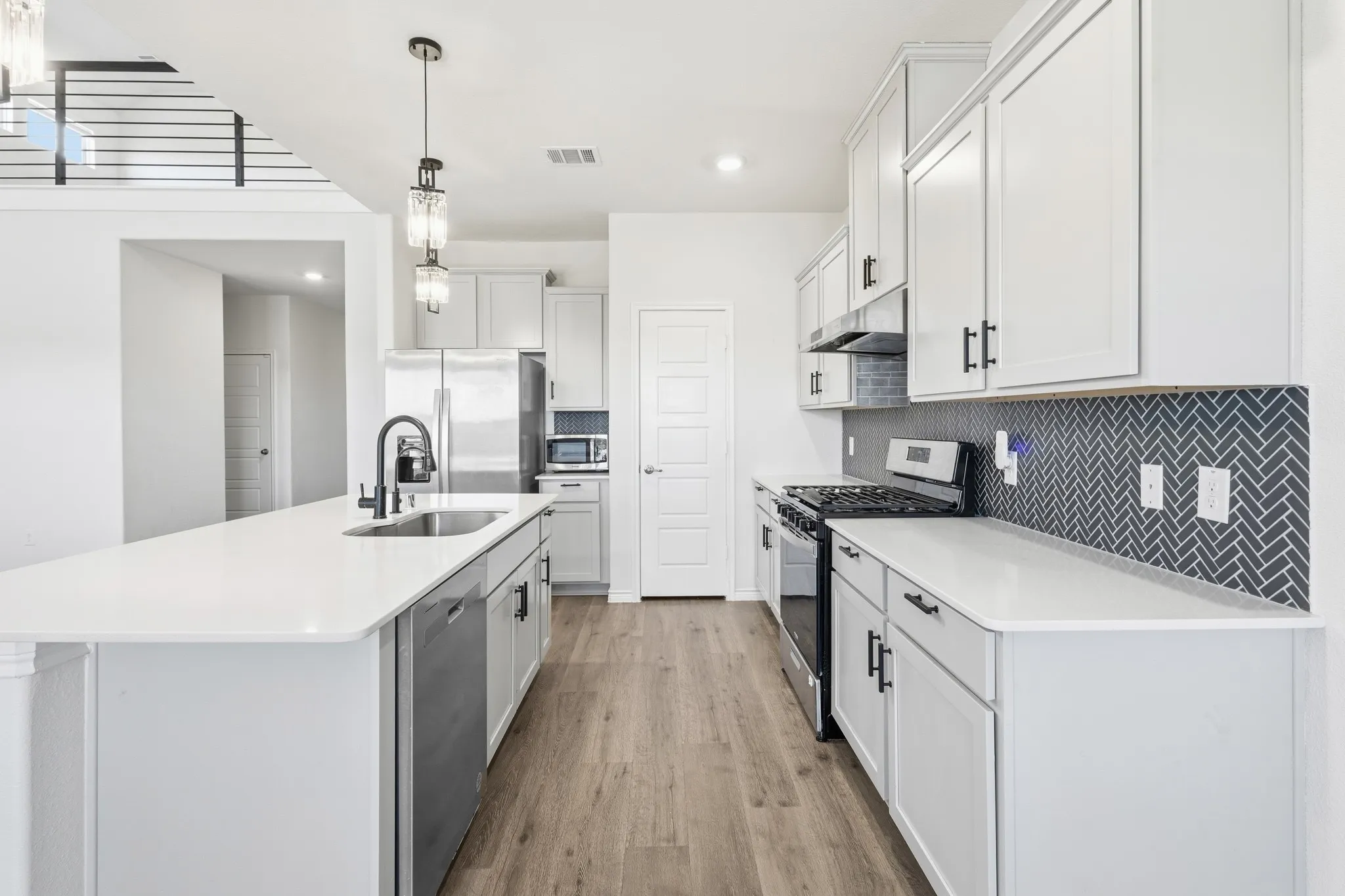 Modern kitchen featuring white cabinetry, a large kitchen island with an integrated sink, stainless steel appliances, wood-finish flooring, and a dark herringbone tile backsplash