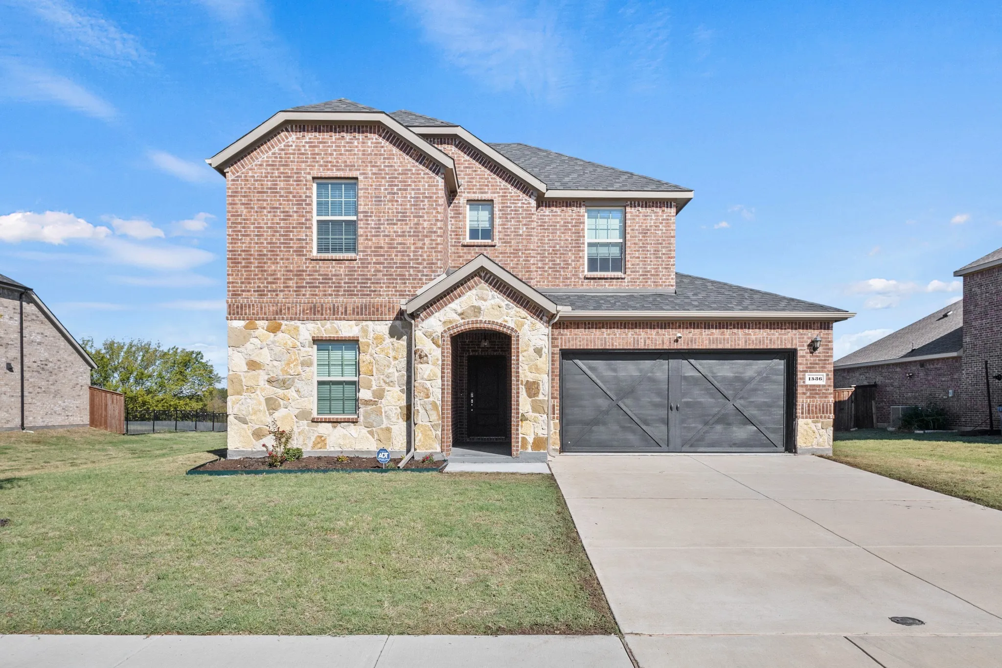 Two-story brick and stone facade, arched entry, dark garage door with decorative trim, concrete driveway, and manicured front lawn