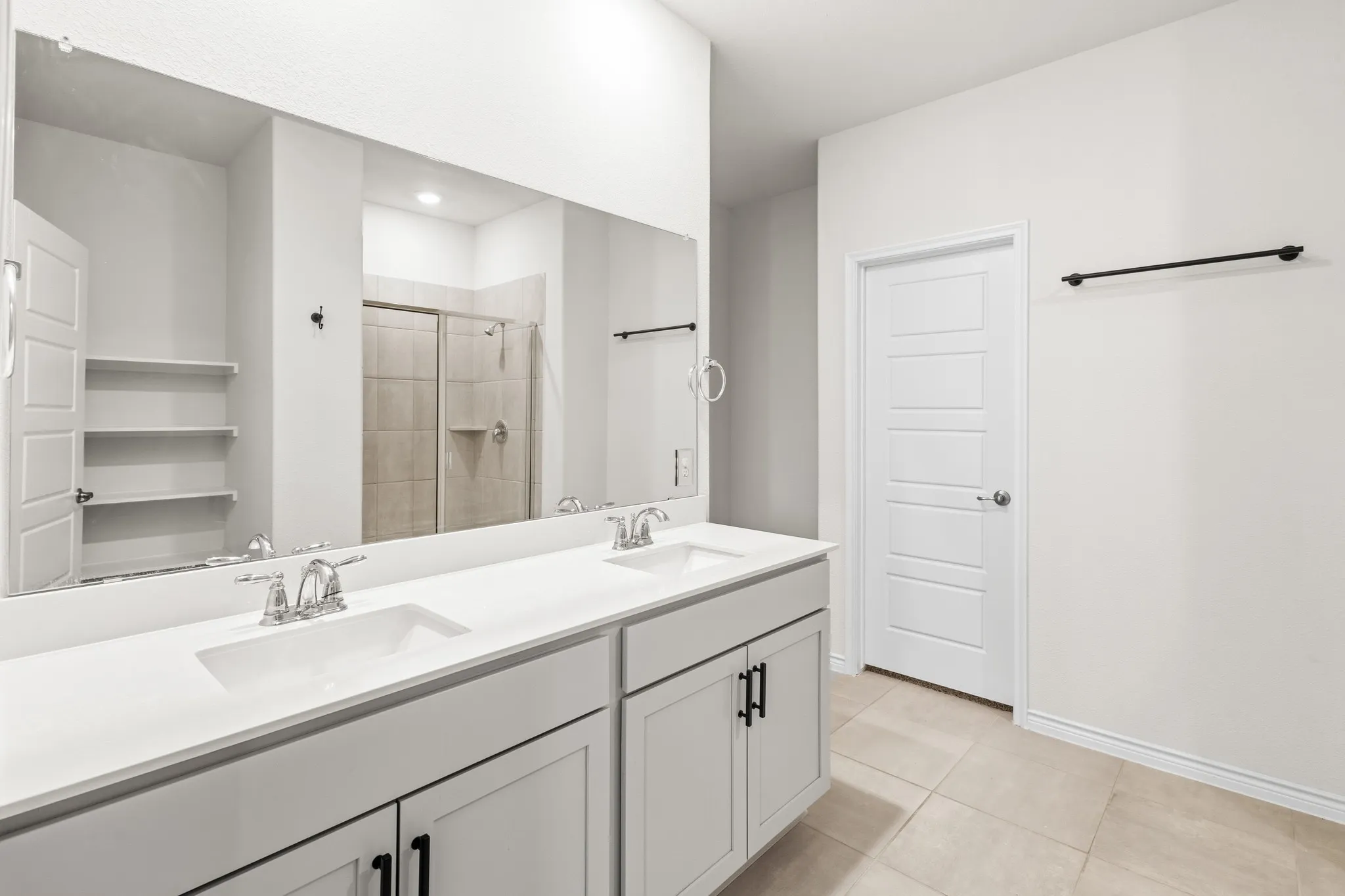 Dual vanity with integrated sinks, expansive wall mirror, and light-toned tile flooring