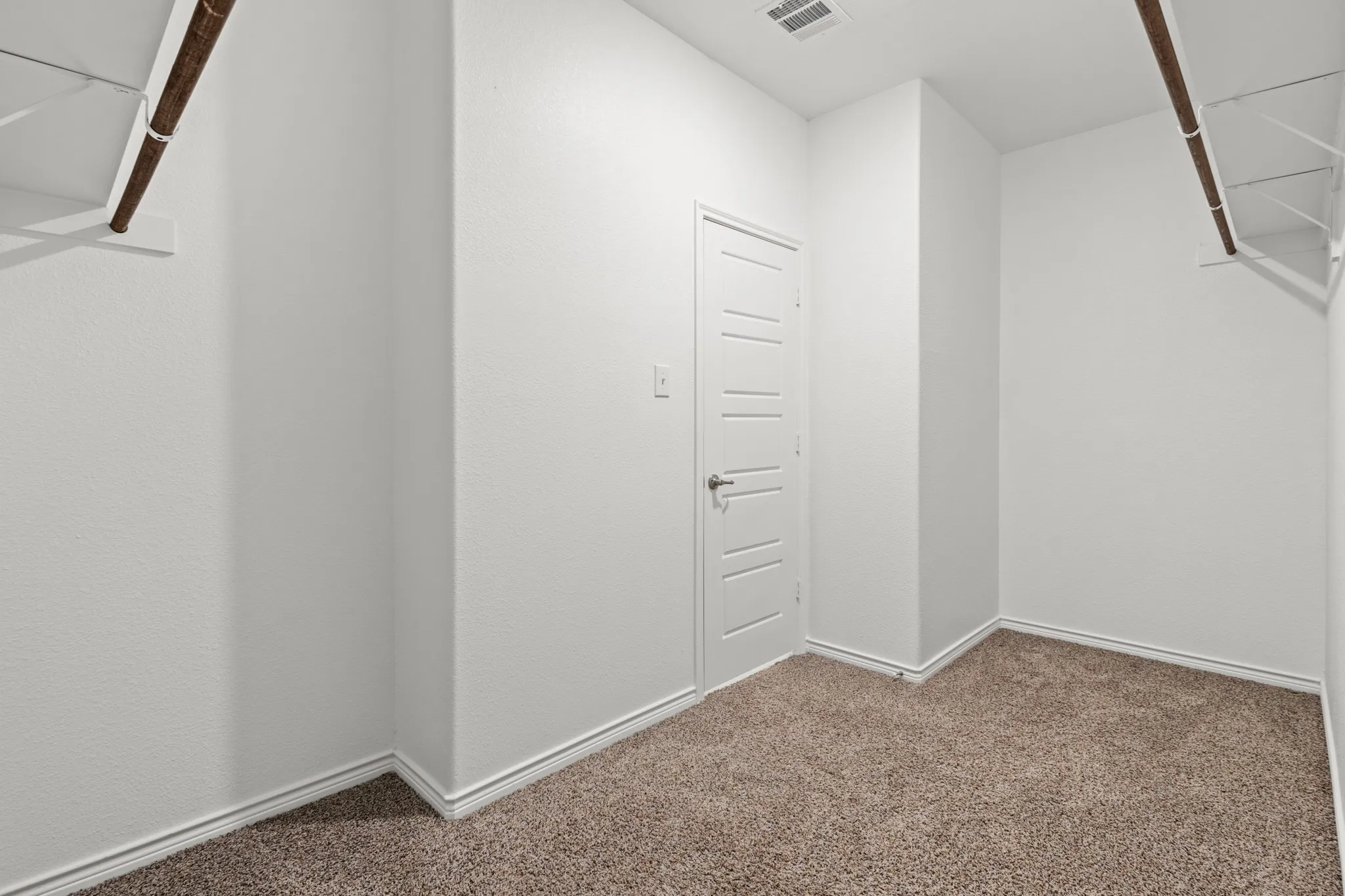 Plush carpet flooring, white walls, storage shelving, and a paneled door with a lever handle