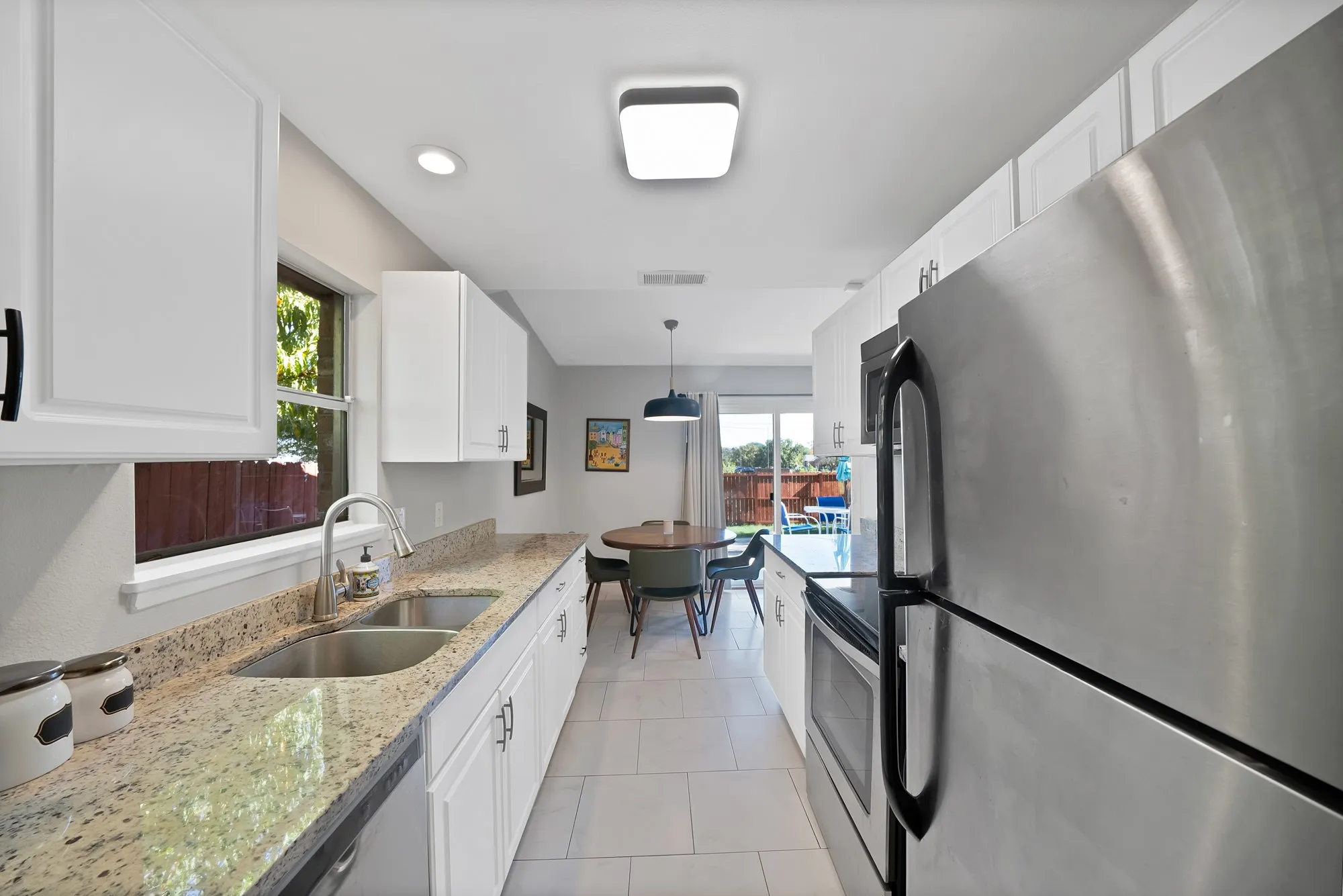 Kitchen with stainless steel appliances, light stone counters, white cabinets, hanging light fixtures, and light tile patterned floors