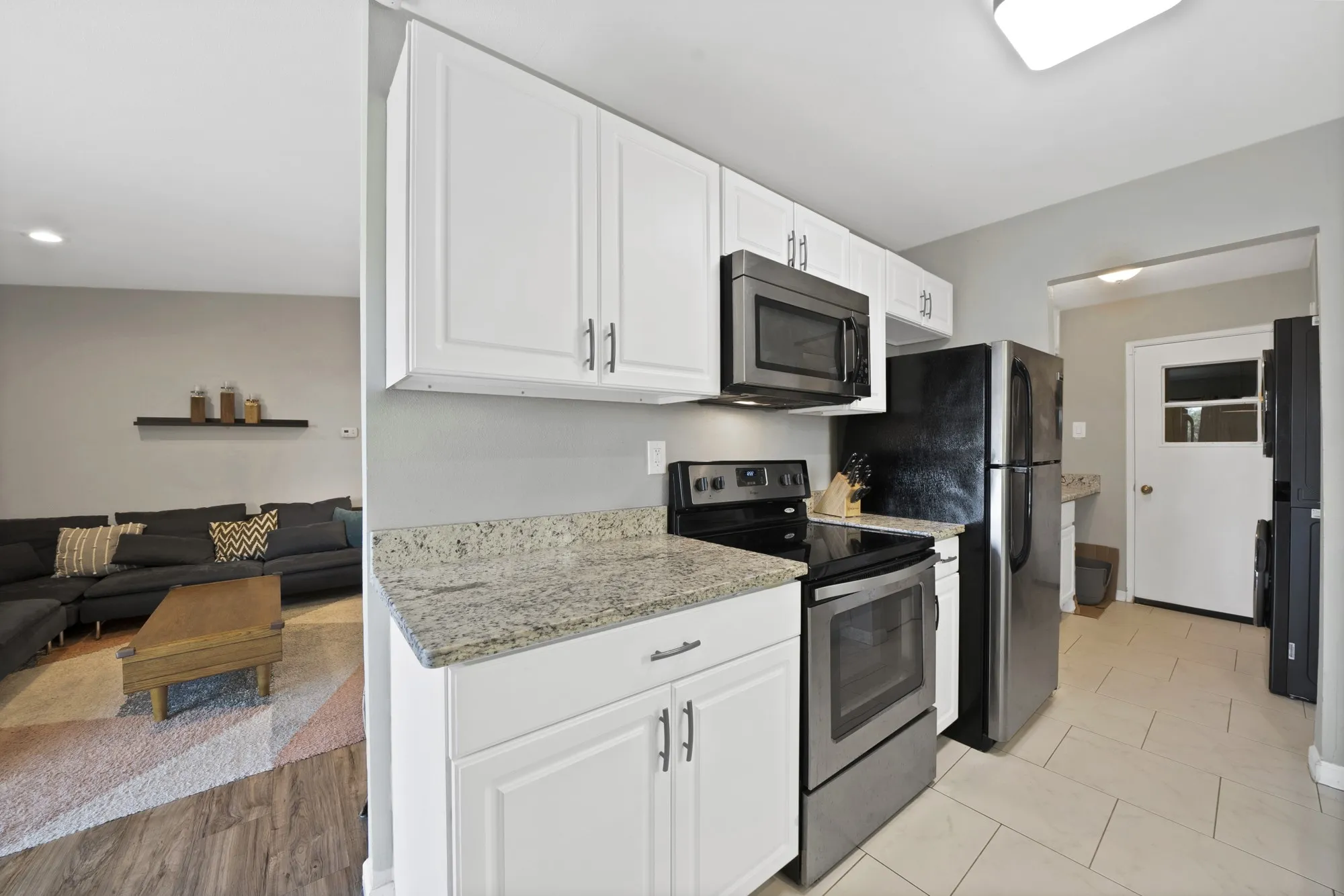 Kitchen featuring appliances with stainless steel finishes, light stone counters, white cabinetry, open floor plan, and washer / clothes dryer
