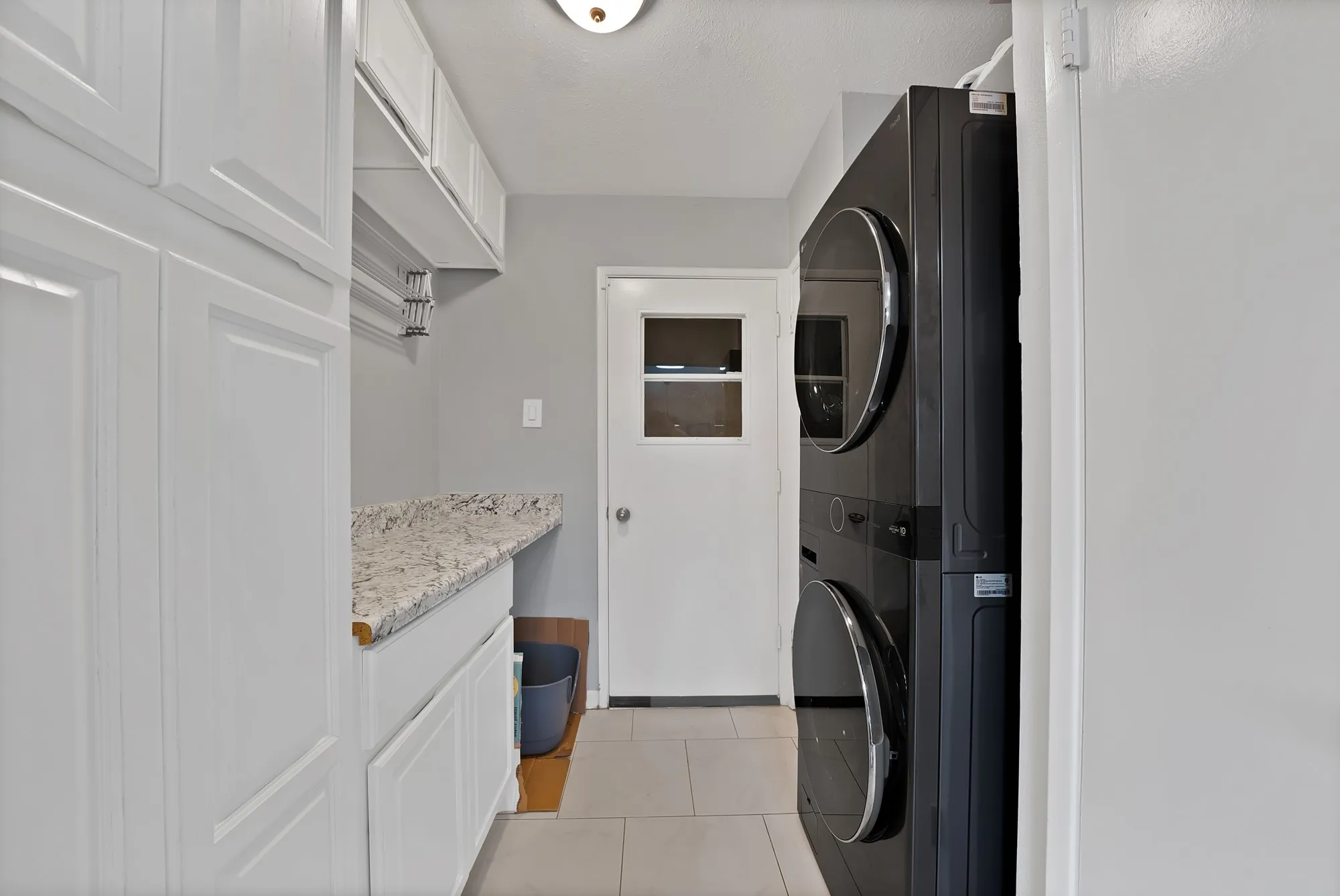 Washroom with light tile patterned floors and stacked washer and clothes dryer