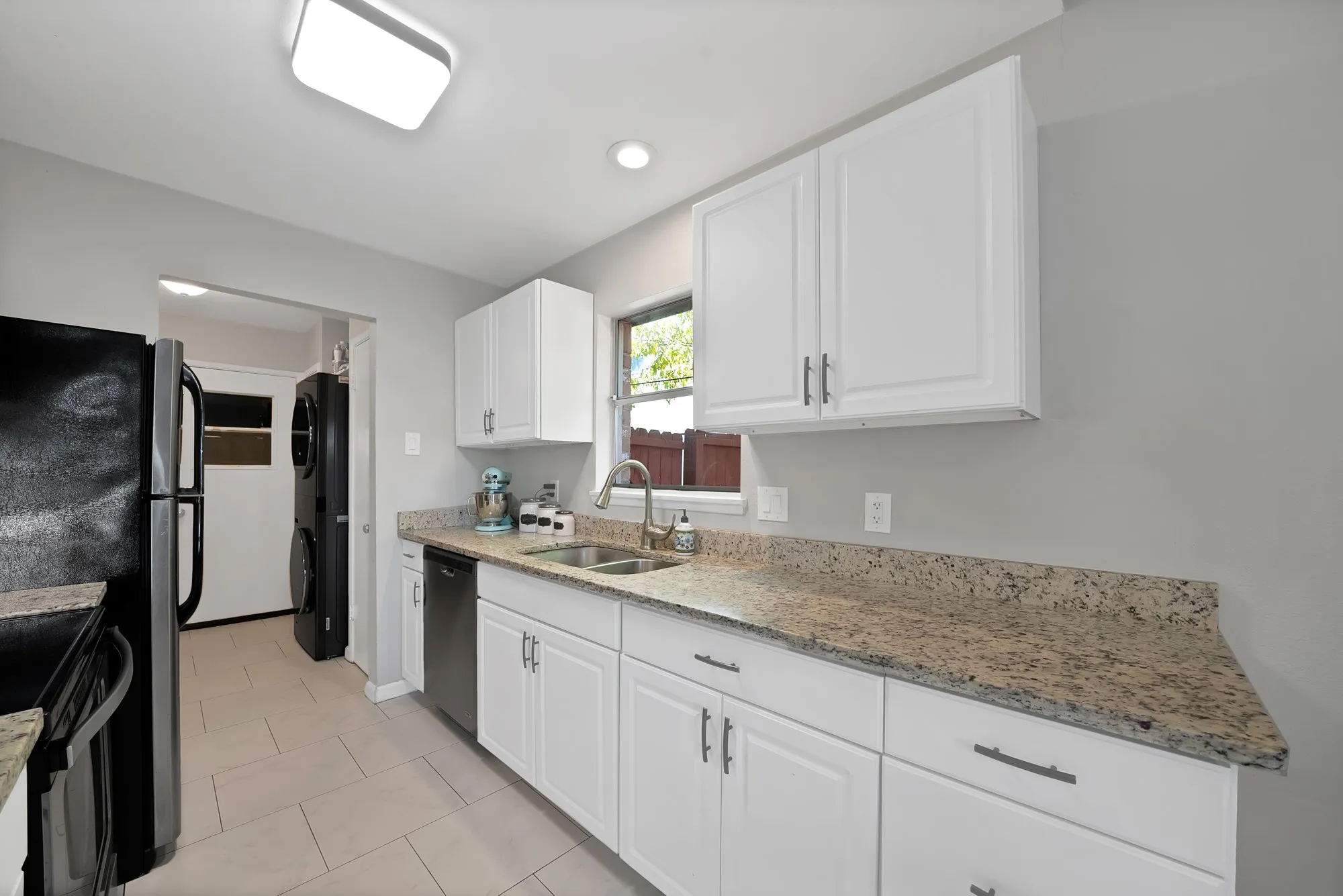 Kitchen featuring light stone counters, white cabinetry, stacked washing machine and dryer, dishwashing machine, and light tile patterned flooring