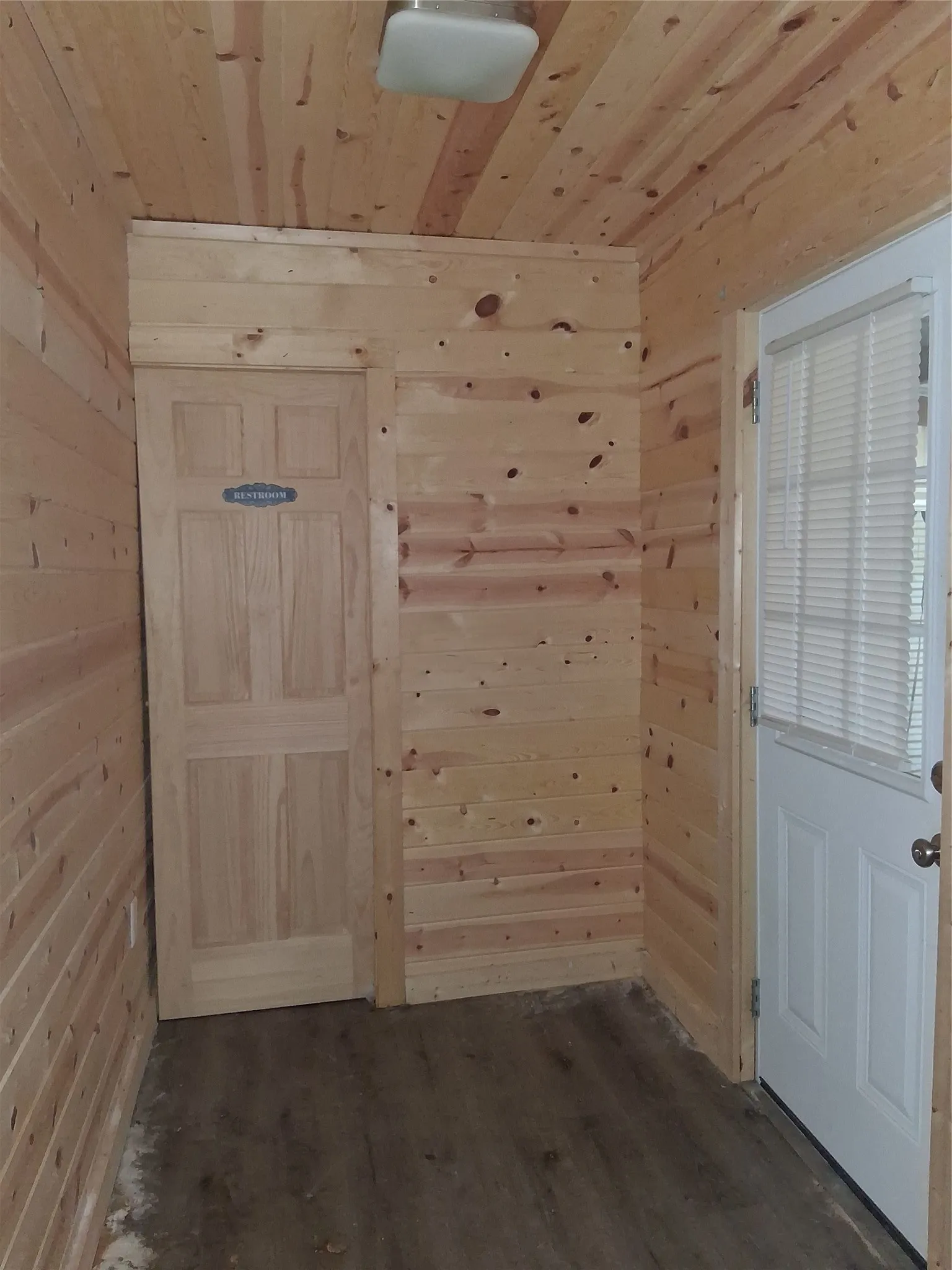 Wood paneling throughout, wood-finish flooring, flush mount lighting, paneled interior door, and exterior door with integrated blinds