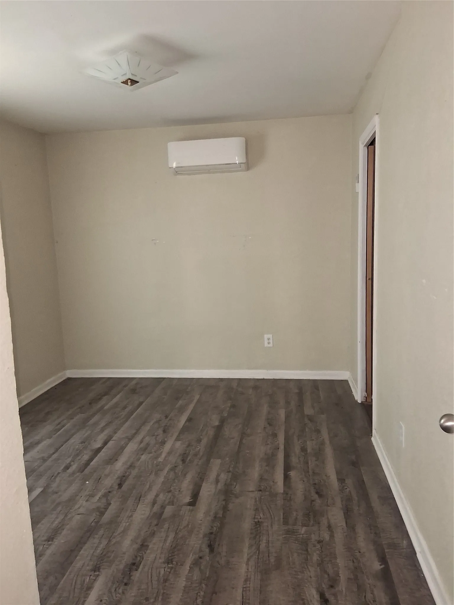 Wood-finish flooring with white baseboards, a wall-mounted mini-split HVAC unit, and a ceiling-mounted light fixture