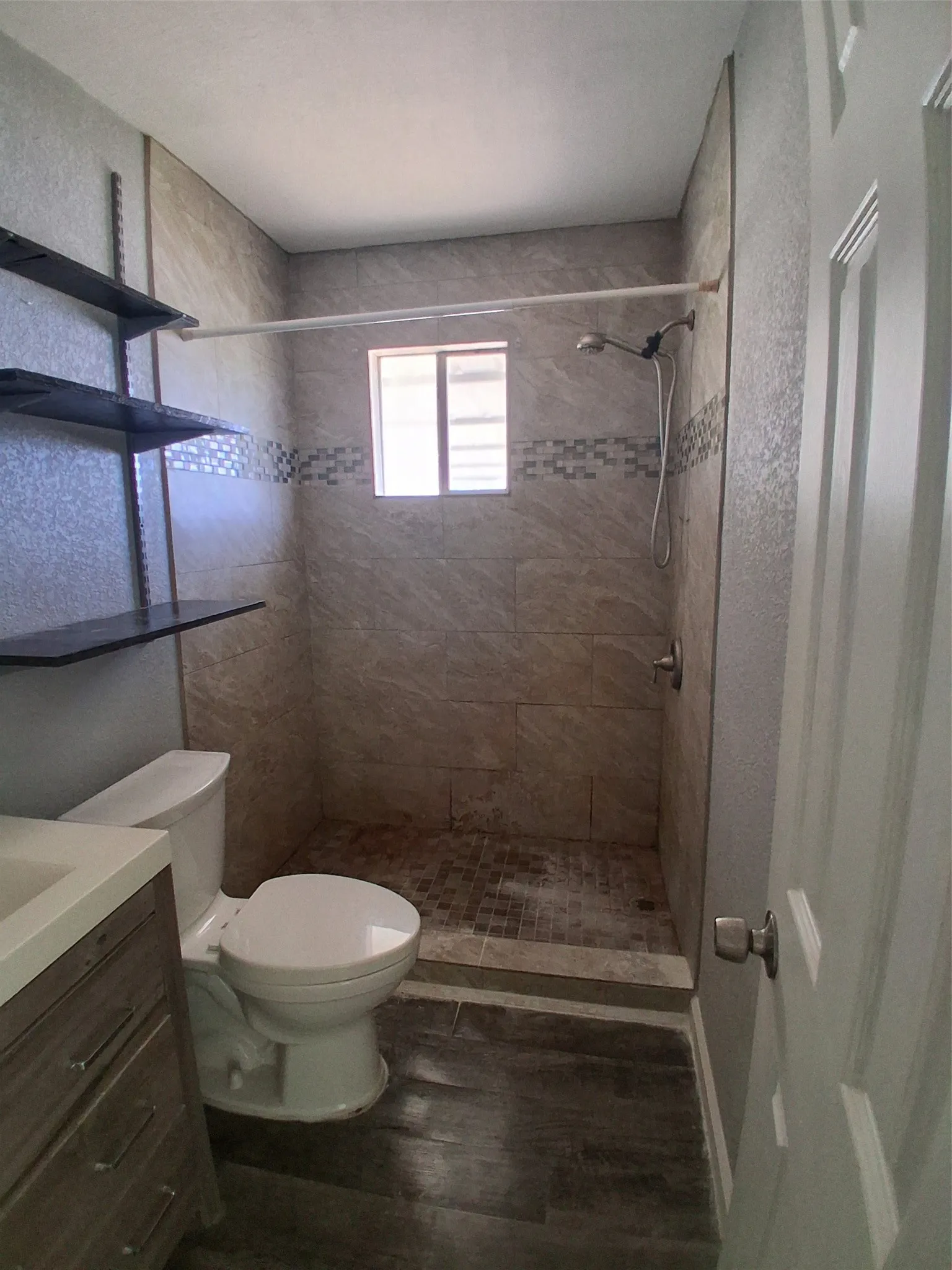 Walk-in shower with full-height wall tiling, mosaic accent band, and a window