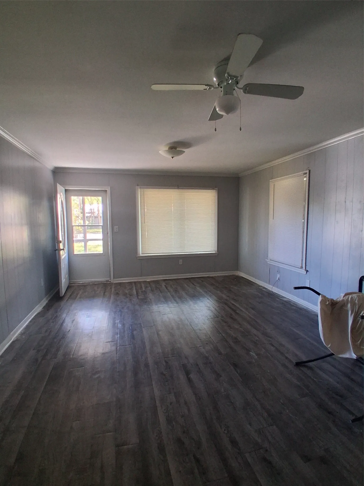 Spacious room featuring wood-finish flooring, light gray paneled walls, and a ceiling fan