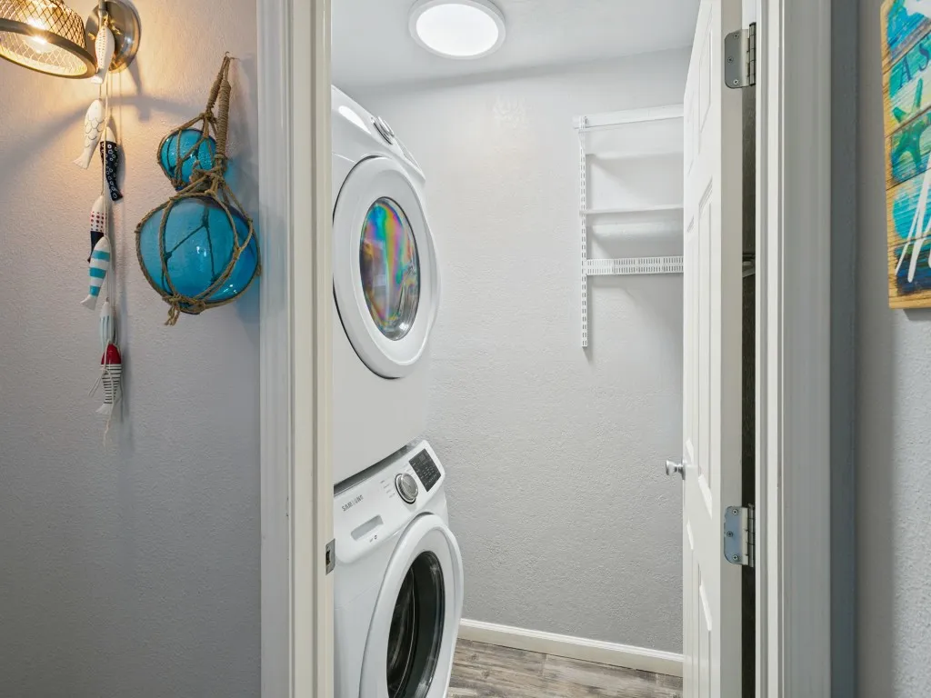 Stacked washer and dryer unit, wood-finish flooring, recessed lighting, and wall-mounted shelving
