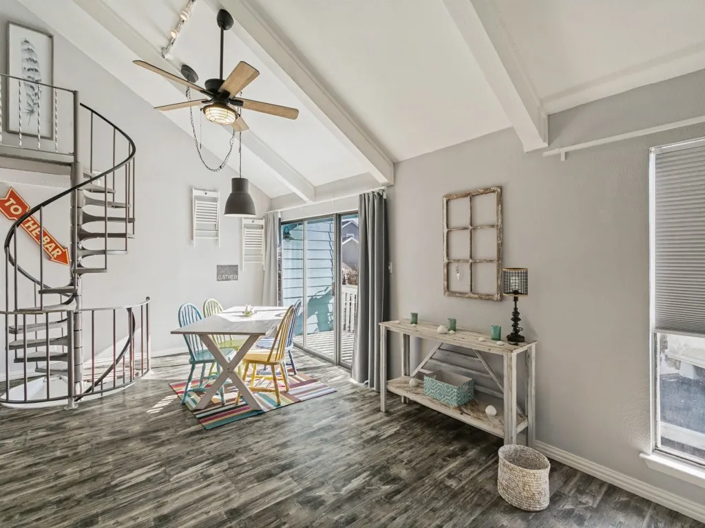 Vaulted ceiling with exposed beams, wood-finish flooring, black spiral staircase, and sliding glass door