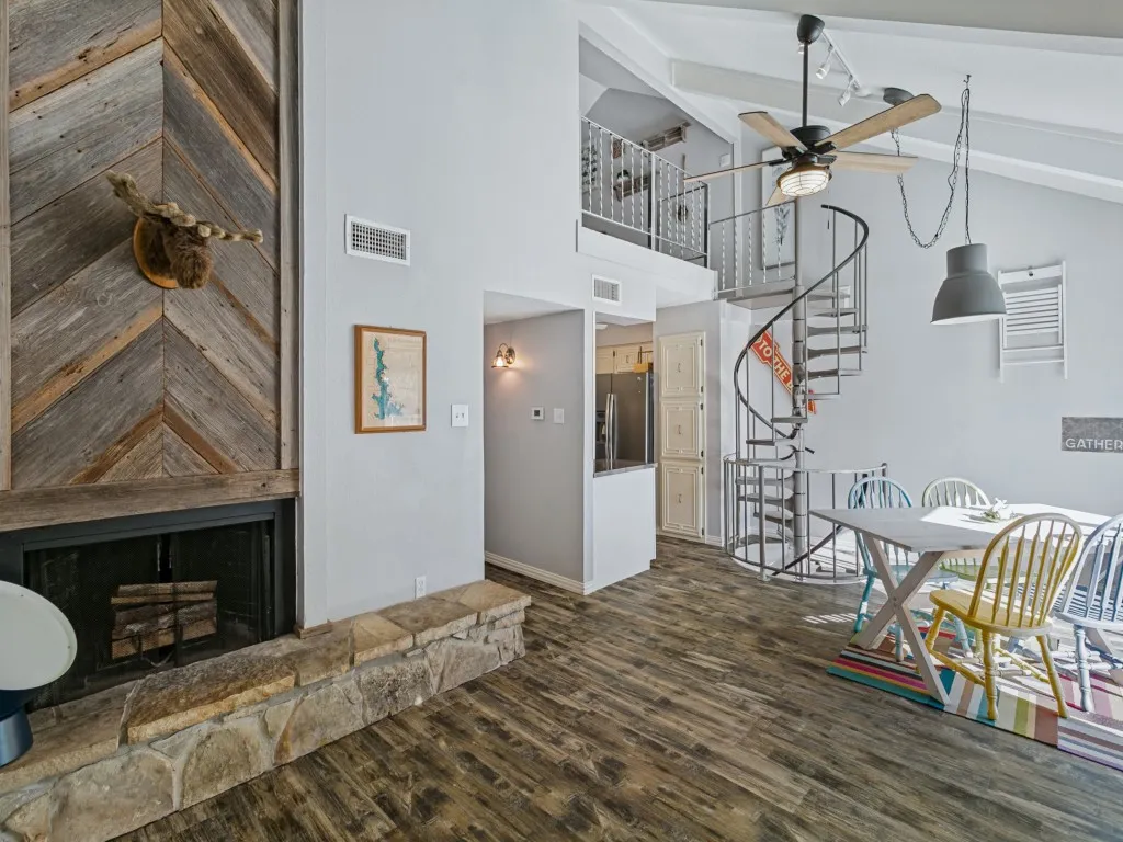 Vaulted ceiling, wood-finish flooring, stone fireplace with a wood-clad surround, spiral staircase, and an open loft area
