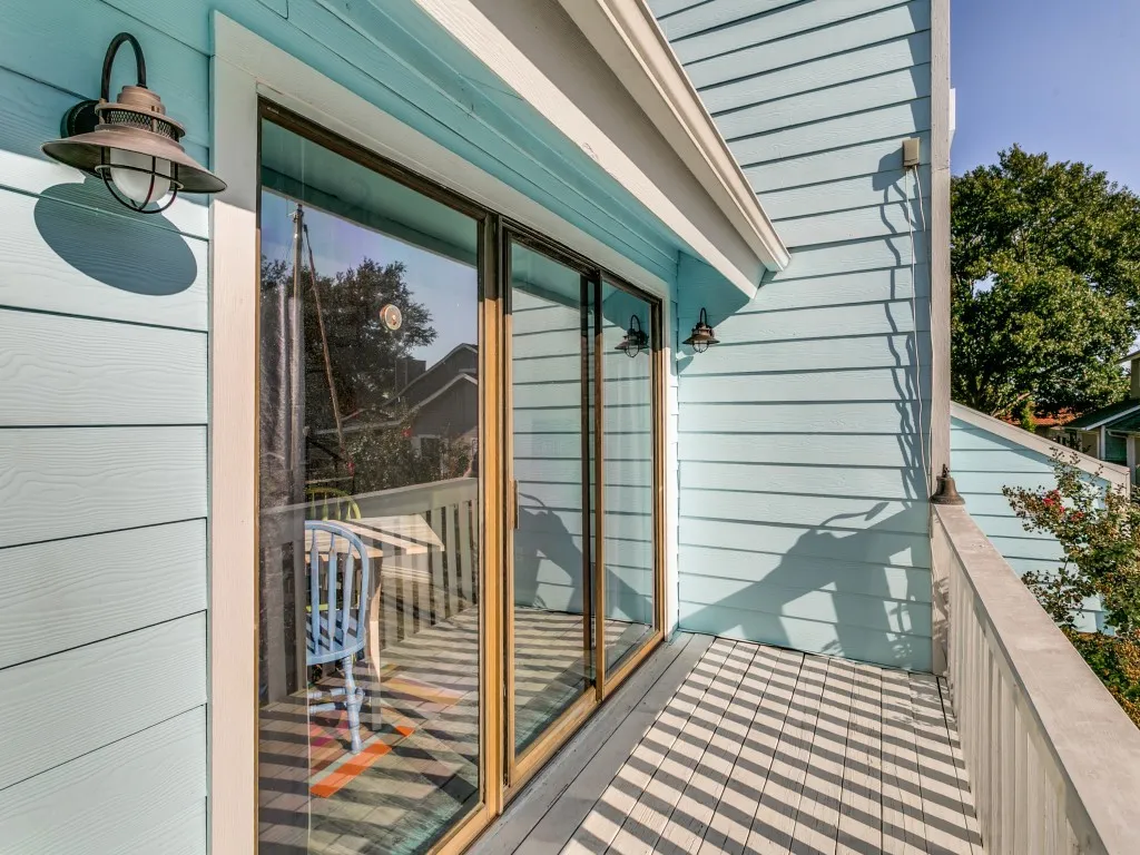 Upper-level balcony featuring a light blue exterior, sliding glass doors, built-in exterior lighting, and a durable railing